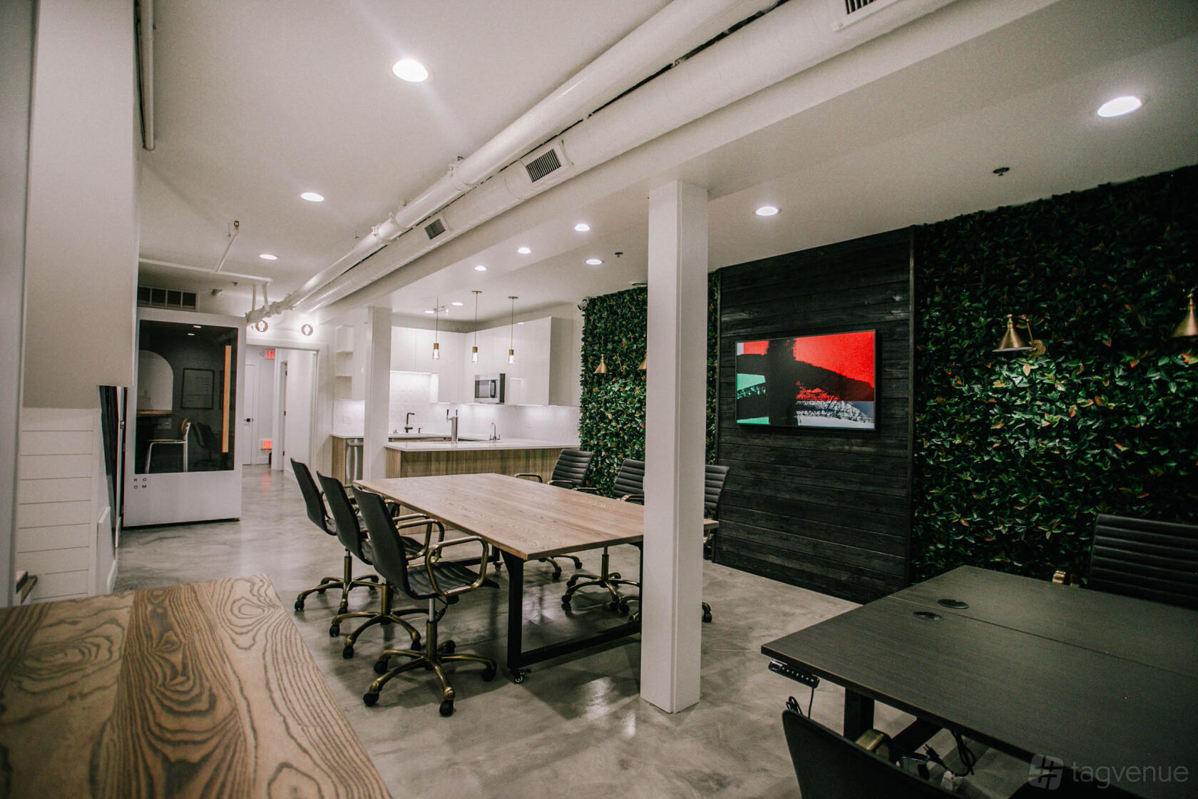 A meeting room with a long wooden table, black chairs, a living plant wall, and built-in kitchenette at Brick & Mortar.