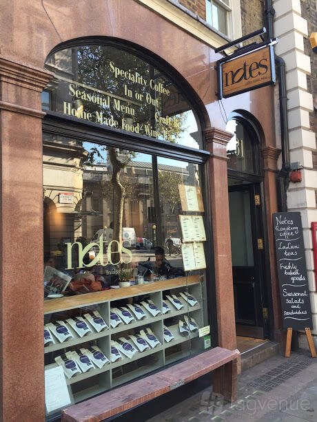 A pub with large arched windows, outdoor menu board, and sidewalk seating at Notes Coffee & Bars Trafalgar Square.