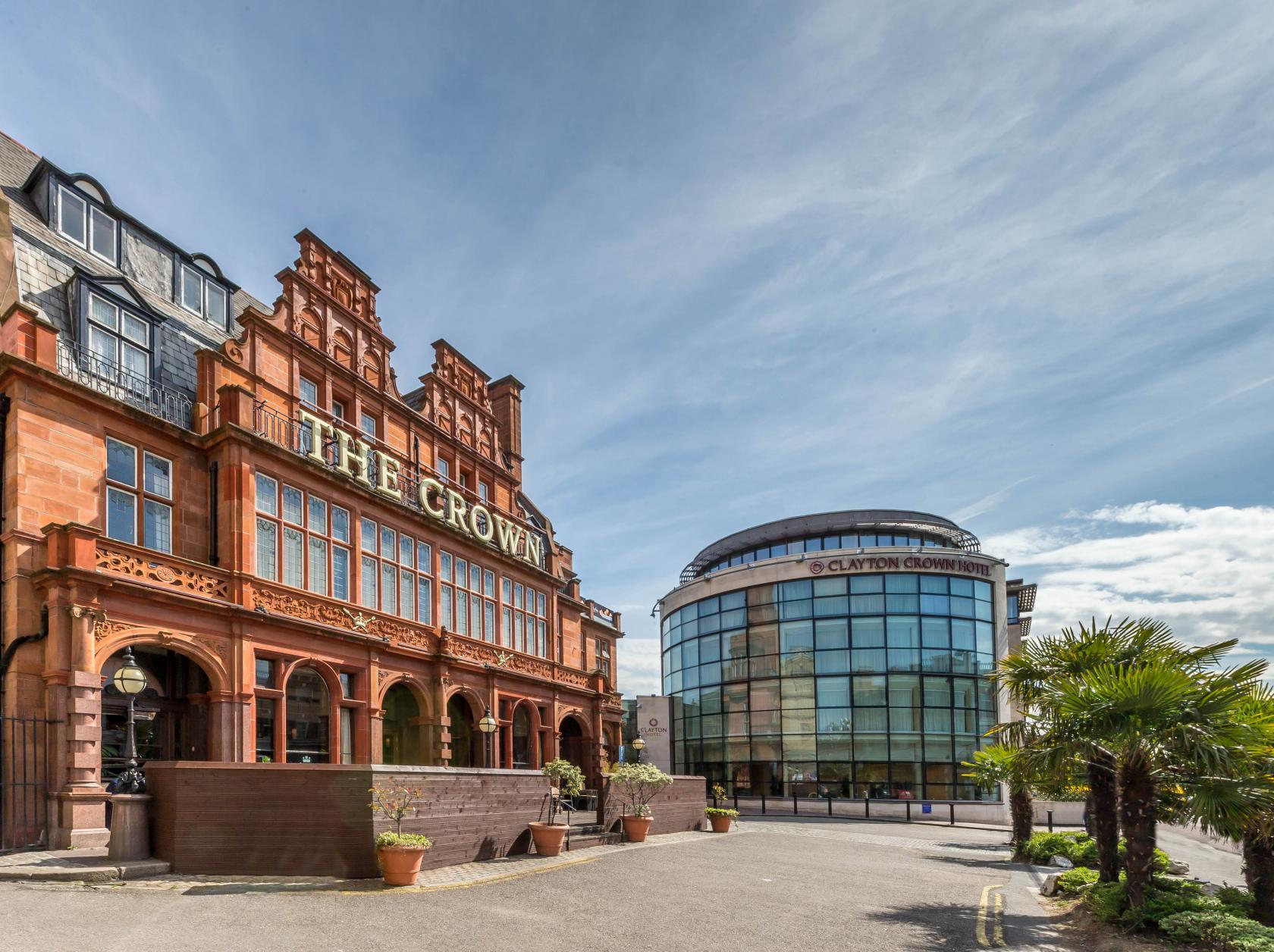 A hotel with ornate red brick facade and arched windows beside a modern glass building at The Crown London Hotel.