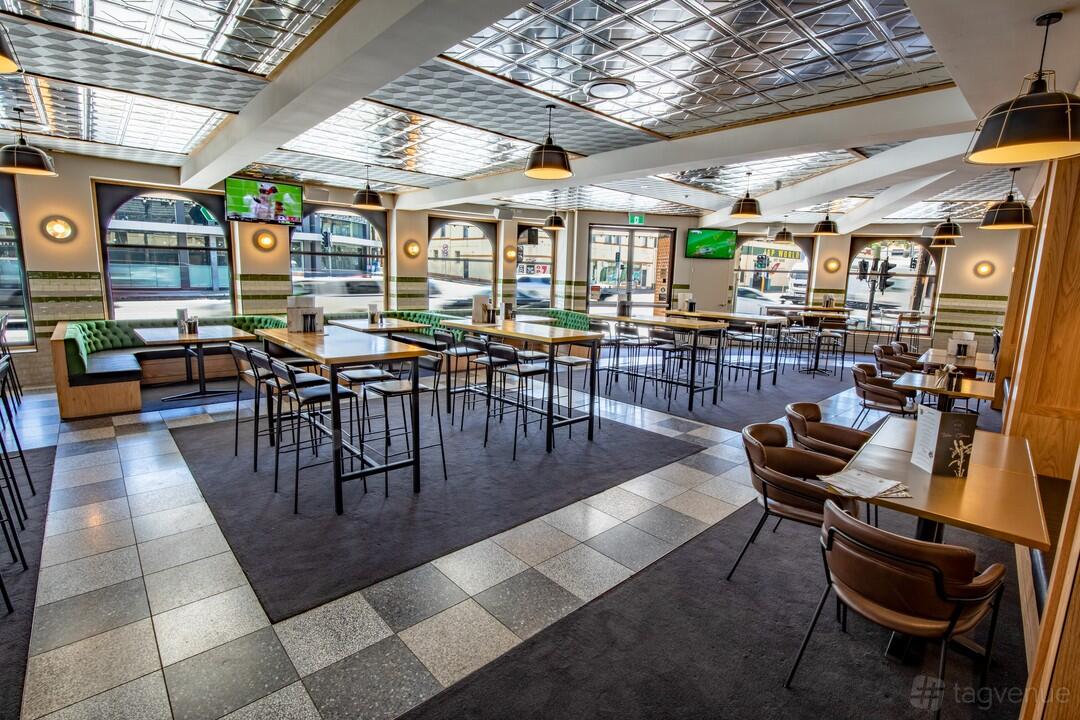 A hotel bar with green upholstered booth seating, high tables, and large windows at Southern Cross Hotel.