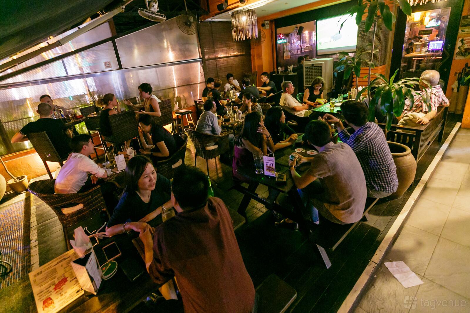 A restaurant terrace with wicker chairs, wooden tables, greenery, and ambient lighting at Georges Madbar & Grill (Siglap).