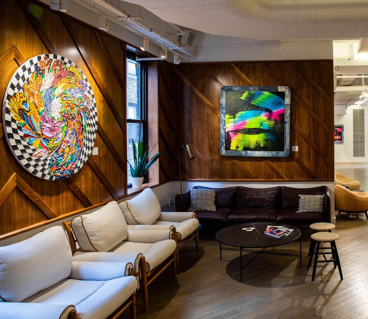 A meeting room with wood paneled walls, colorful abstract art, and seating including sofas and armchairs at Blender Space.