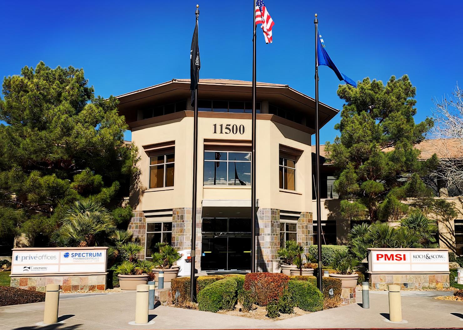 A meeting centre with a stone-accented entrance, American flagpoles, and surrounding trees at OFFICENEST - HENDERSON.