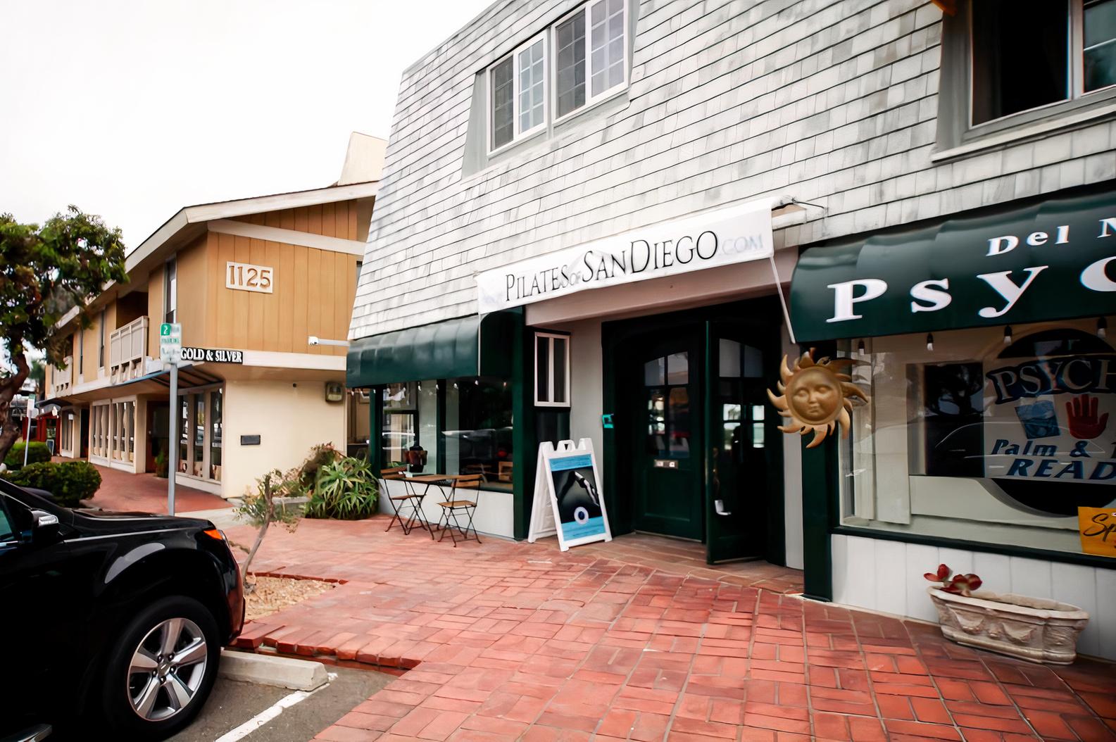 A dance studio with a gray shingle facade, white trim, and large street-facing windows at Pilates of San Diego - Del Mar.