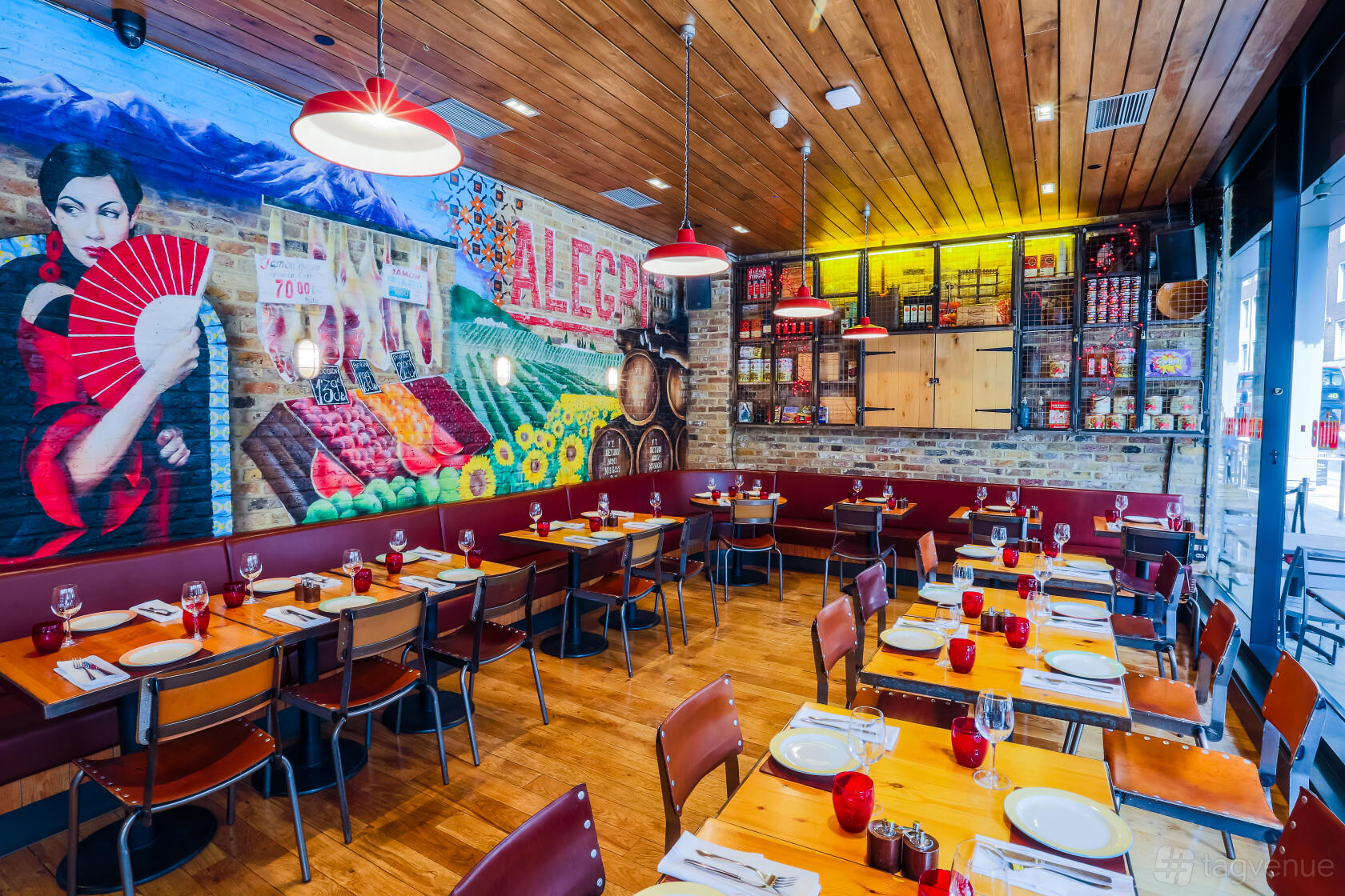 A restaurant dining room with a colorful mural, wood ceiling, pendant lights, and set tables at Camino Monument.