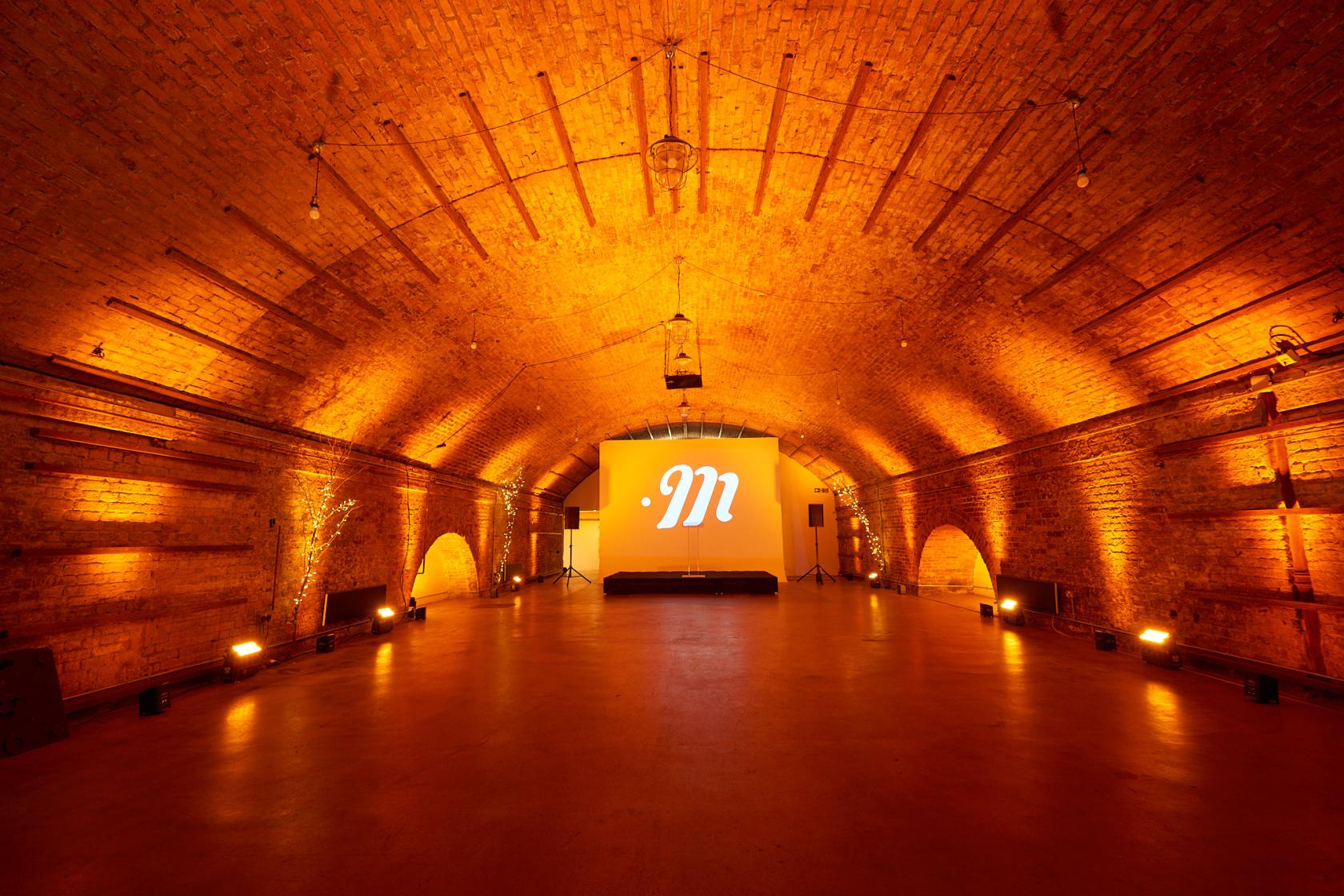 An event venue with exposed brick vaulted ceilings and dramatic uplighting at Motel Studios.