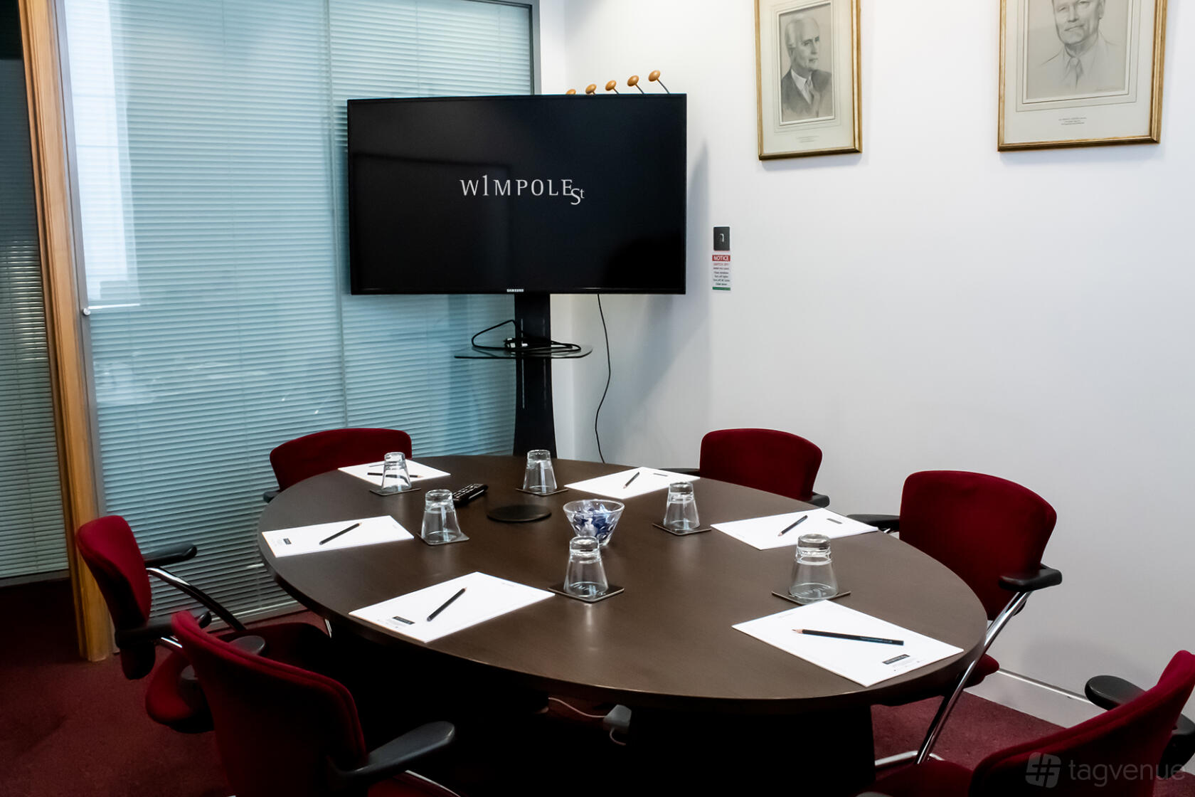 A meeting room with a dark oval table, red chairs, notepads, and a large monitor at 1 Wimpole Street.