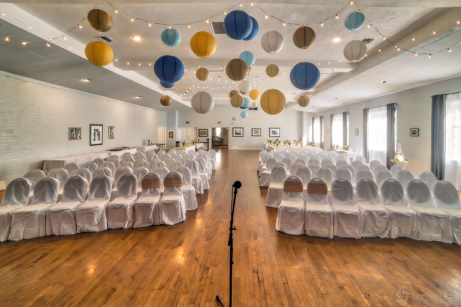 A community centre with wooden floors, rows of white chair covers, string lights, and paper lanterns at Woman's Club of Hollywood.