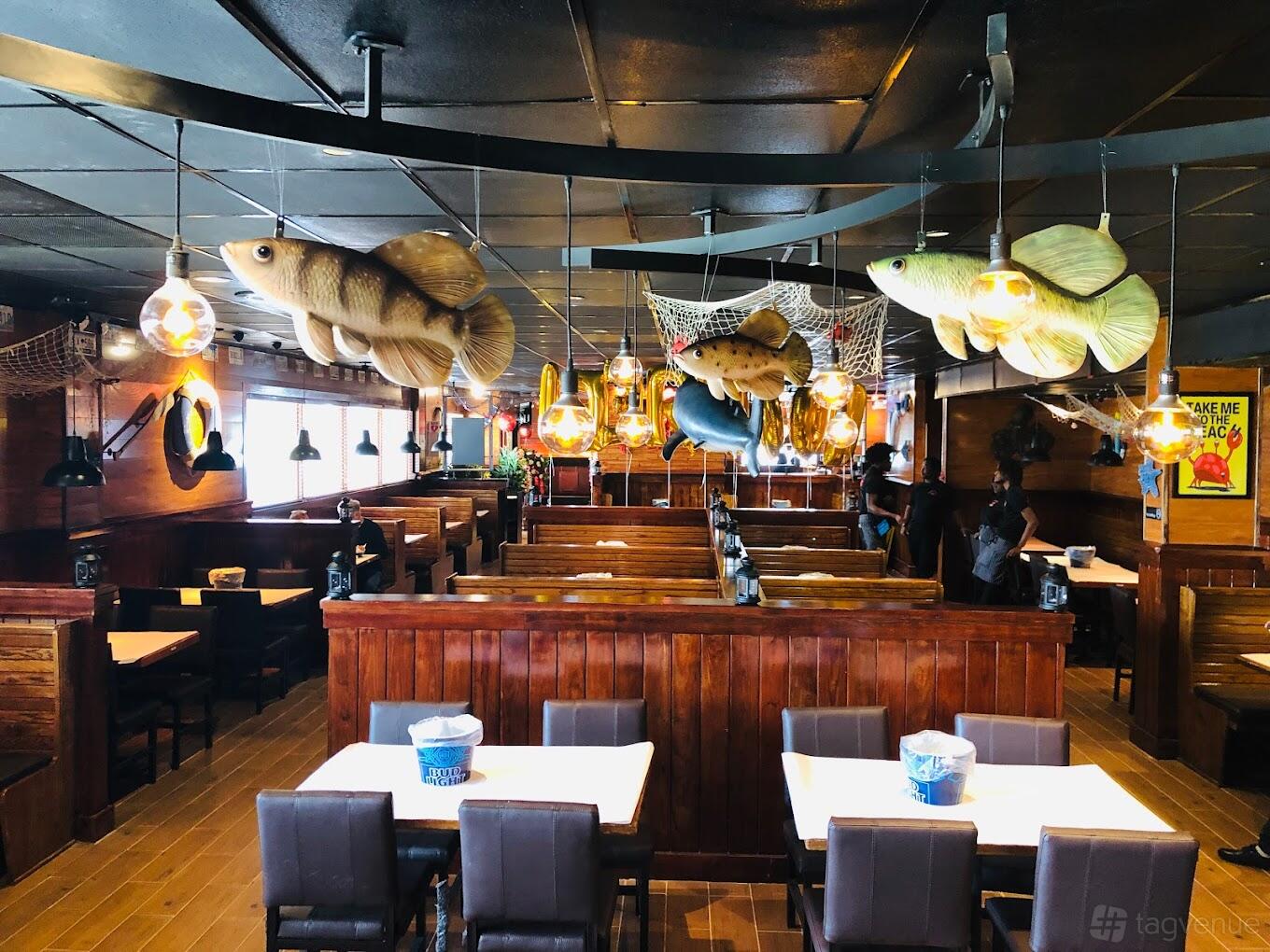 A restaurant dining area with wooden booths, nautical decor, and hanging fish sculptures at Hook & Reel- Pembroke Pines.