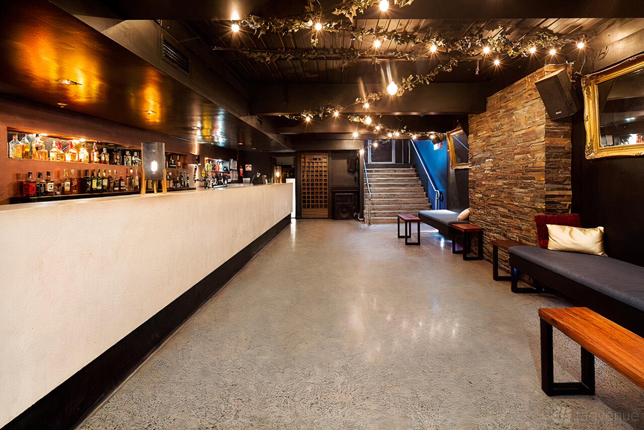 A function room with a long bar, string lights, stone accent wall, and bench seating at La Di Da.