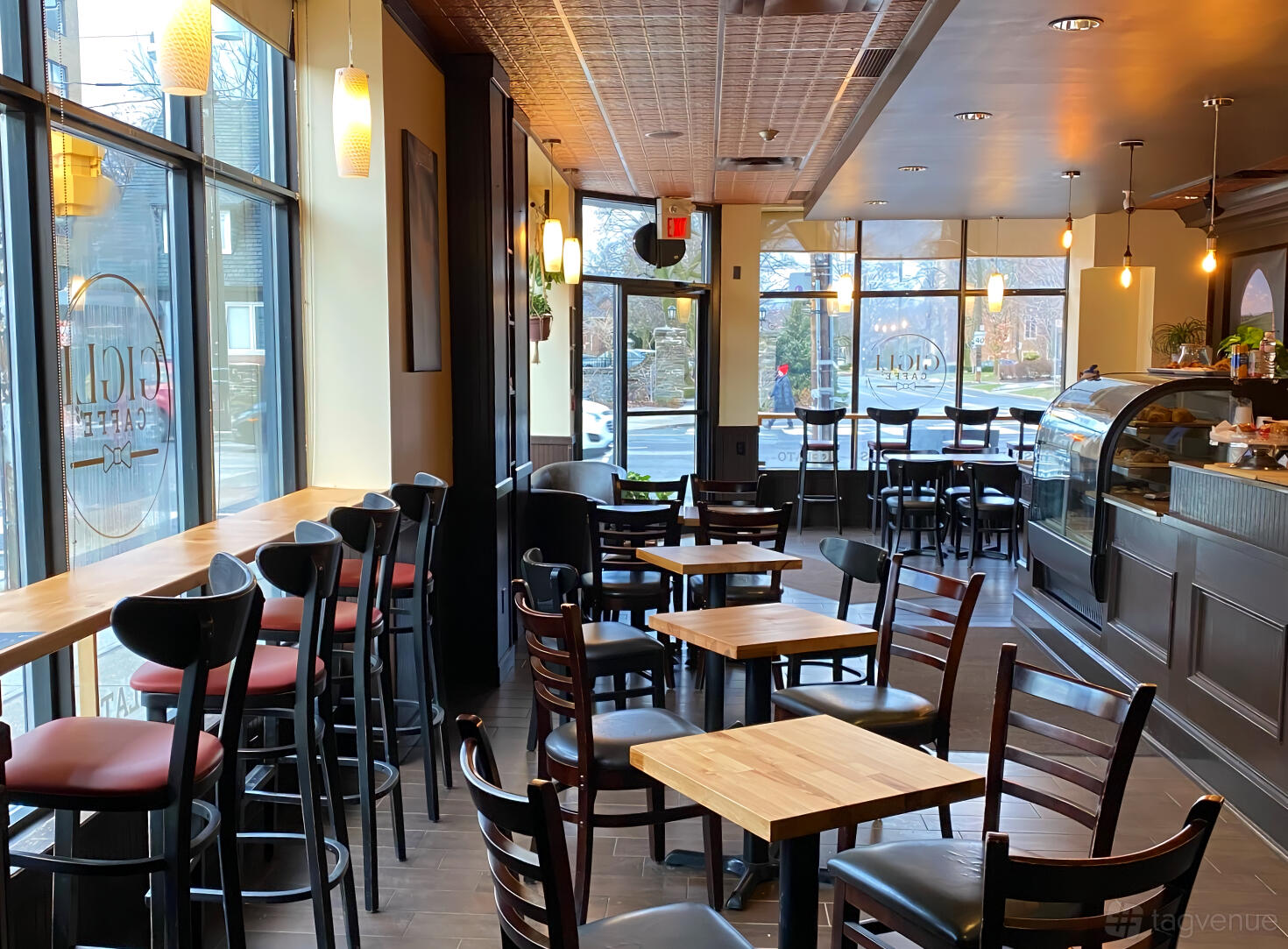 A cafe with floor-to-ceiling windows, wooden tables, and a glass display counter at Gigli Caffe.