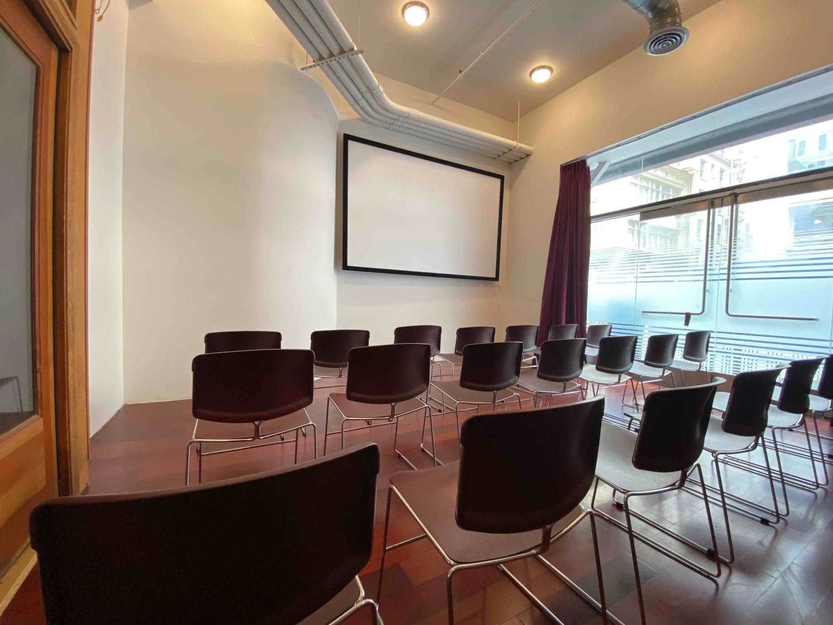 A meeting room with rows of black chairs, a large projection screen, and floor-to-ceiling windows at Club Parlaey.