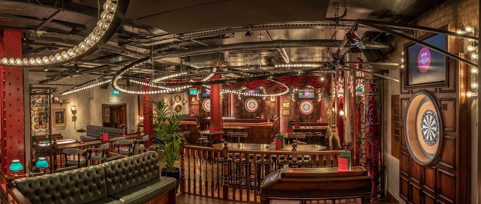 An event space in a bar with dartboards, string lights, red drapery, and wooden tables at Flight Club Birmingham.