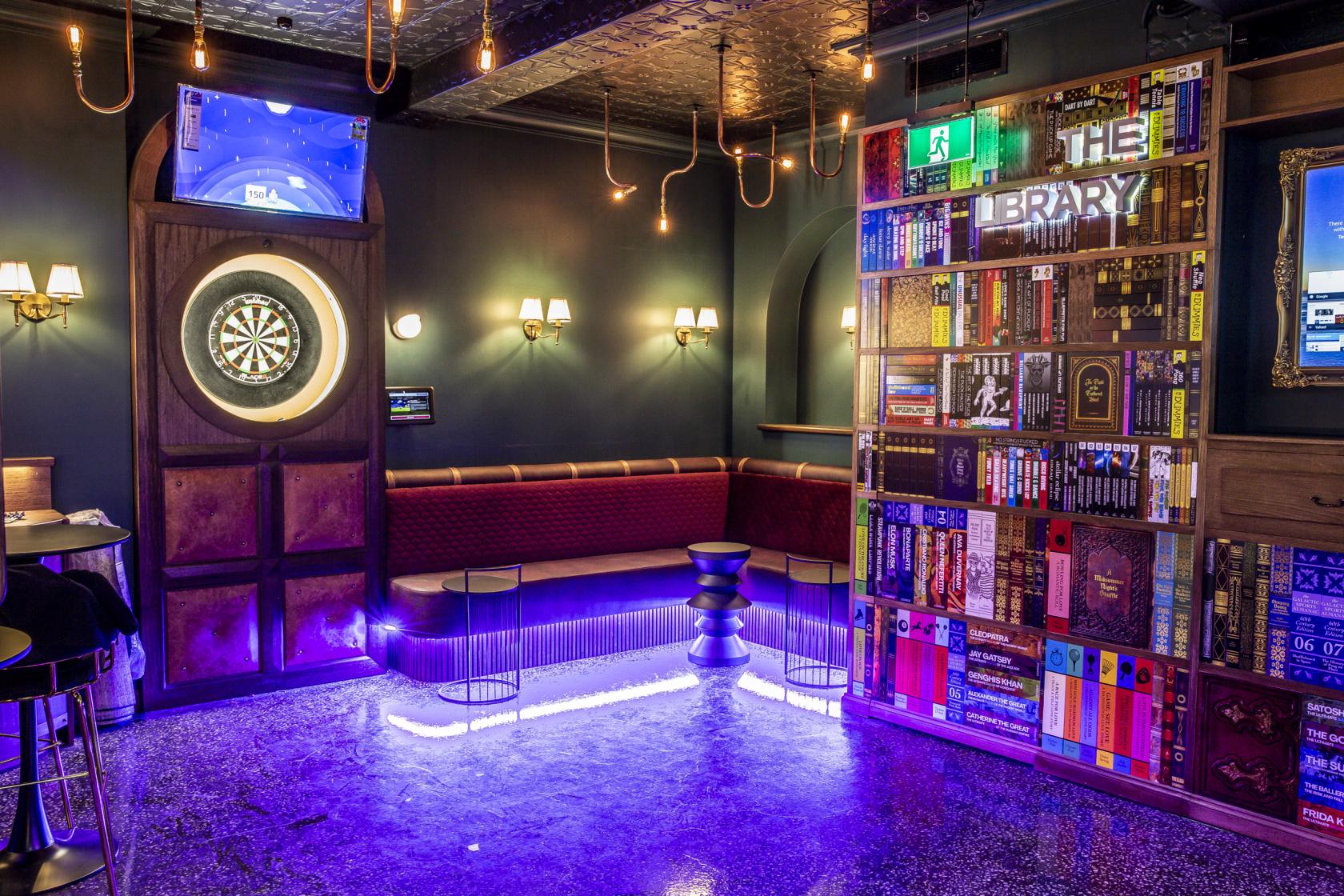 An event space in a bar with a neon-lit bench, dartboard, and bookcase wall at Ballers Clubhouse Carlton.