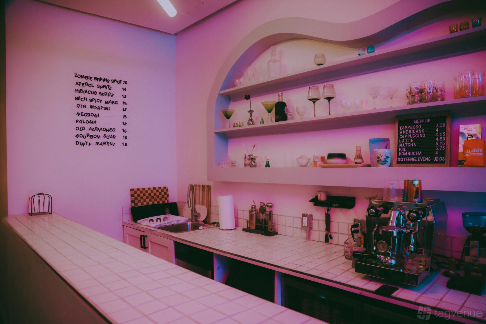An event venue with a tiled countertop, espresso machine, glassware shelves, and pink accent lighting at Sixteen Eleven Studios.