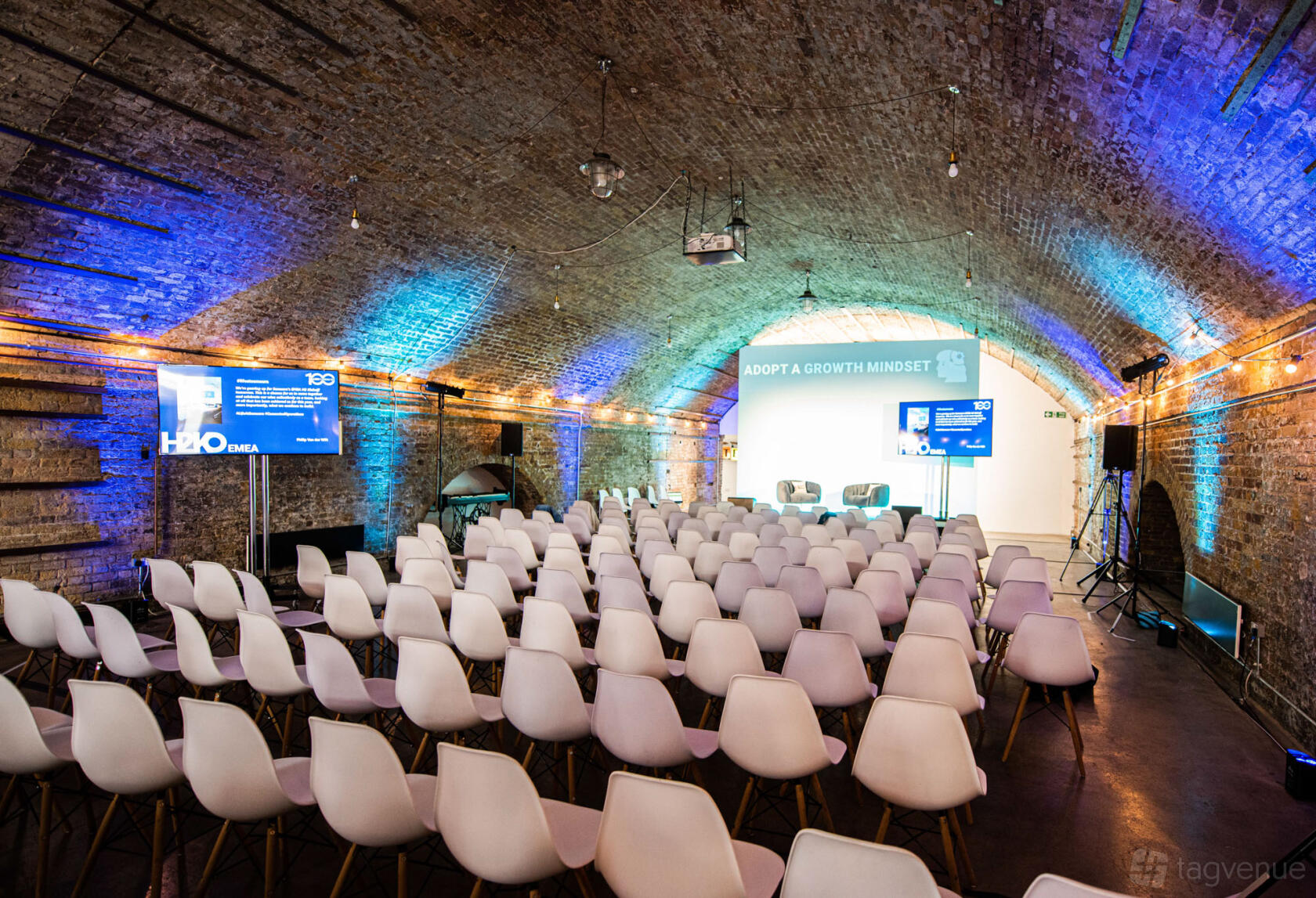 An event venue with arched exposed brick ceiling, rows of white chairs, and stage lighting at Motel Studios.