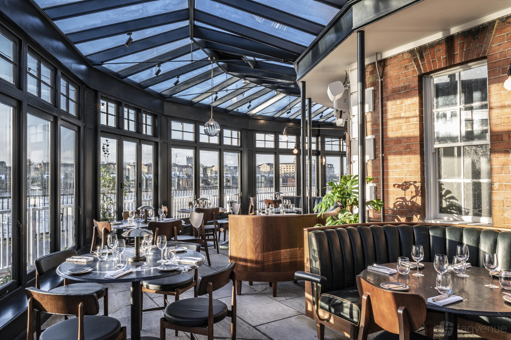 A restaurant with floor-to-ceiling windows, glass roof, and set dining tables at Bread Street Kitchen, Limehouse.