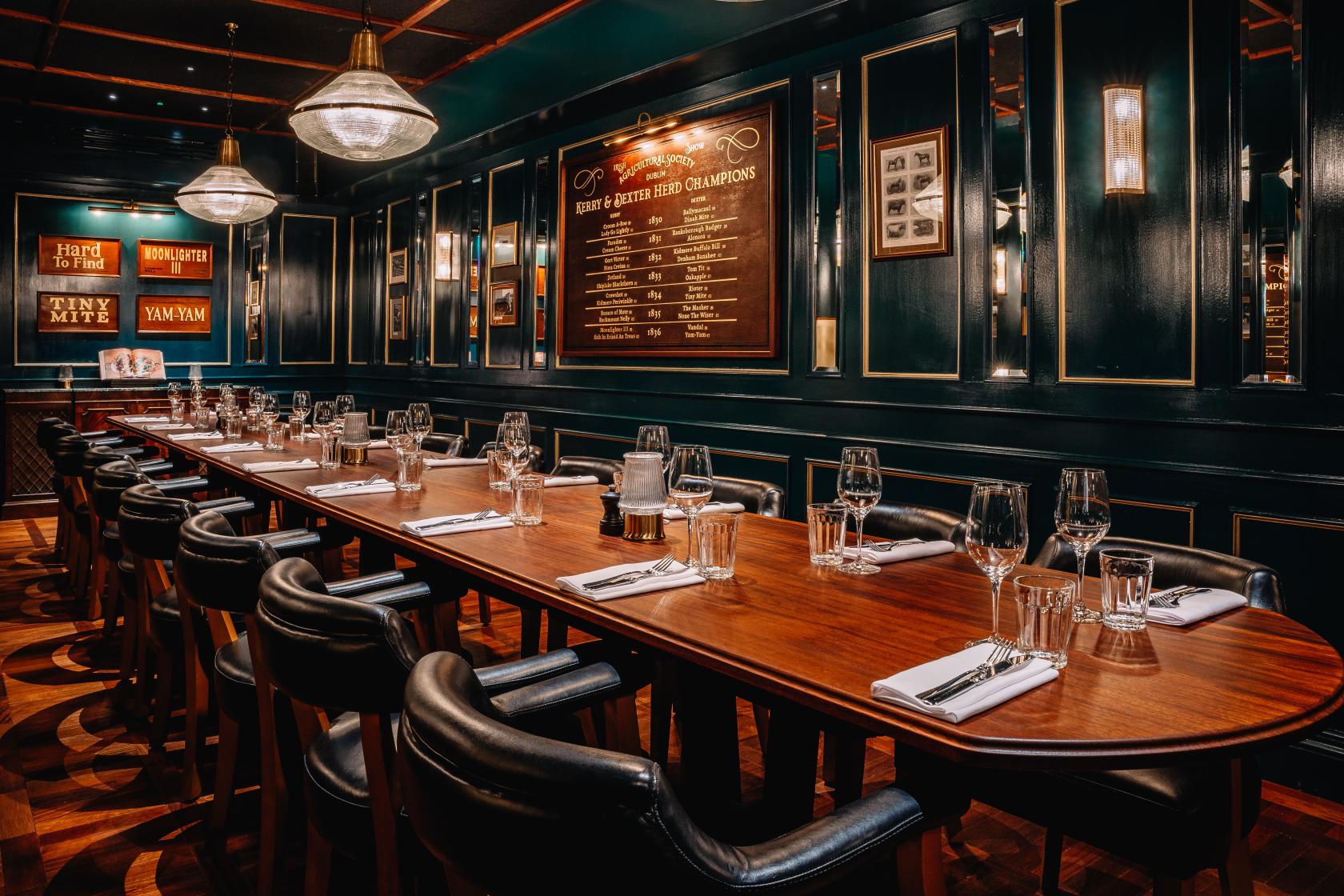 A dining room with a long wooden table, black leather chairs, and dark paneled walls at Hawksmoor.