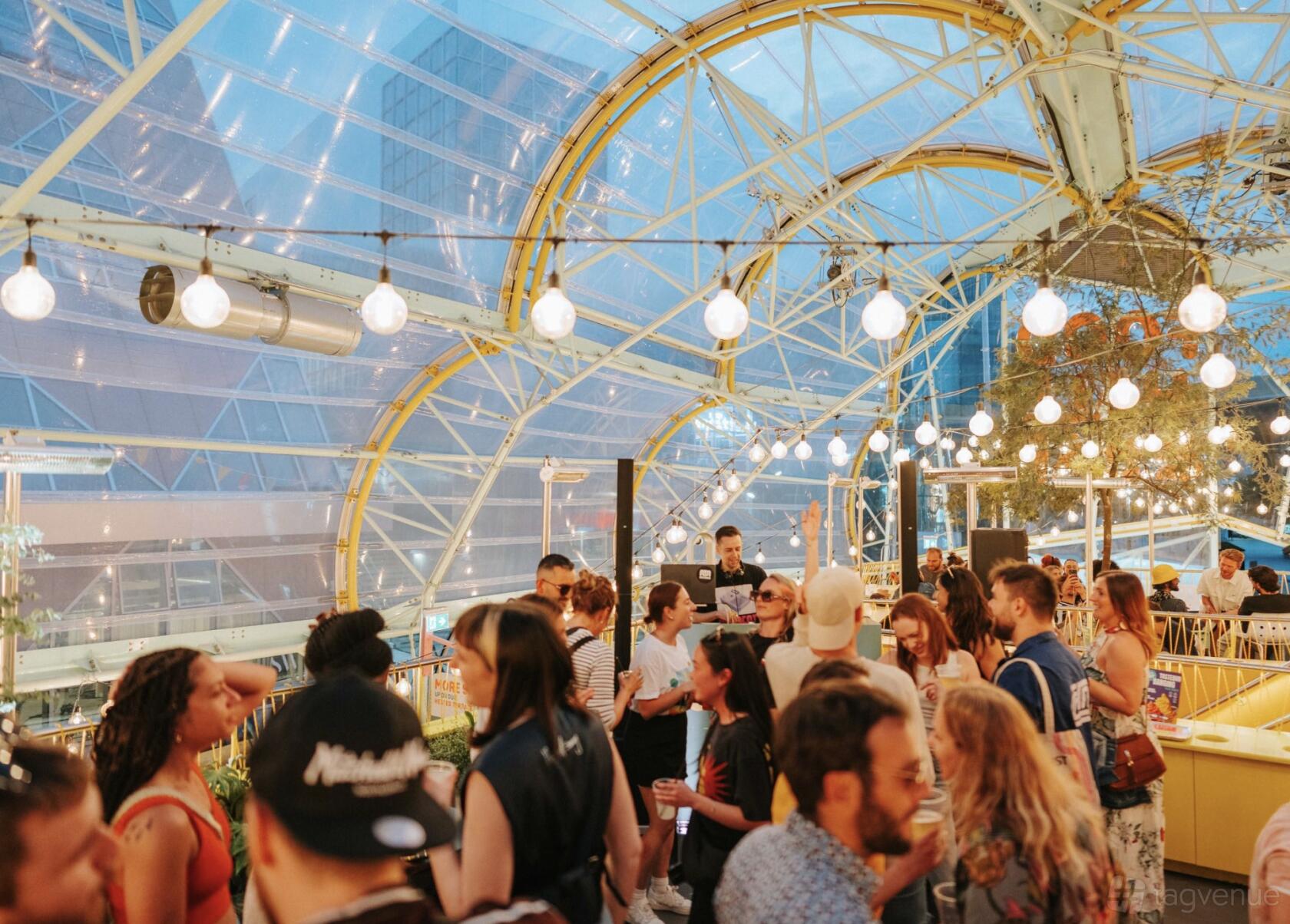 A restaurant with a glass-domed ceiling, exposed metal framework, and hanging string lights at Canteen Food Hall & Bar.