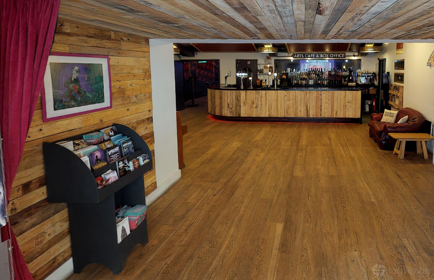 An event venue bar with wood flooring, exposed timber ceiling, and a curved wooden bar at Komedia.