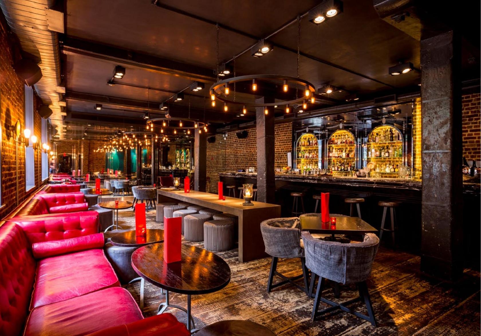 A cocktail bar with red tufted banquettes, exposed brick walls, and a mirrored back bar at Old Bengal Bar.