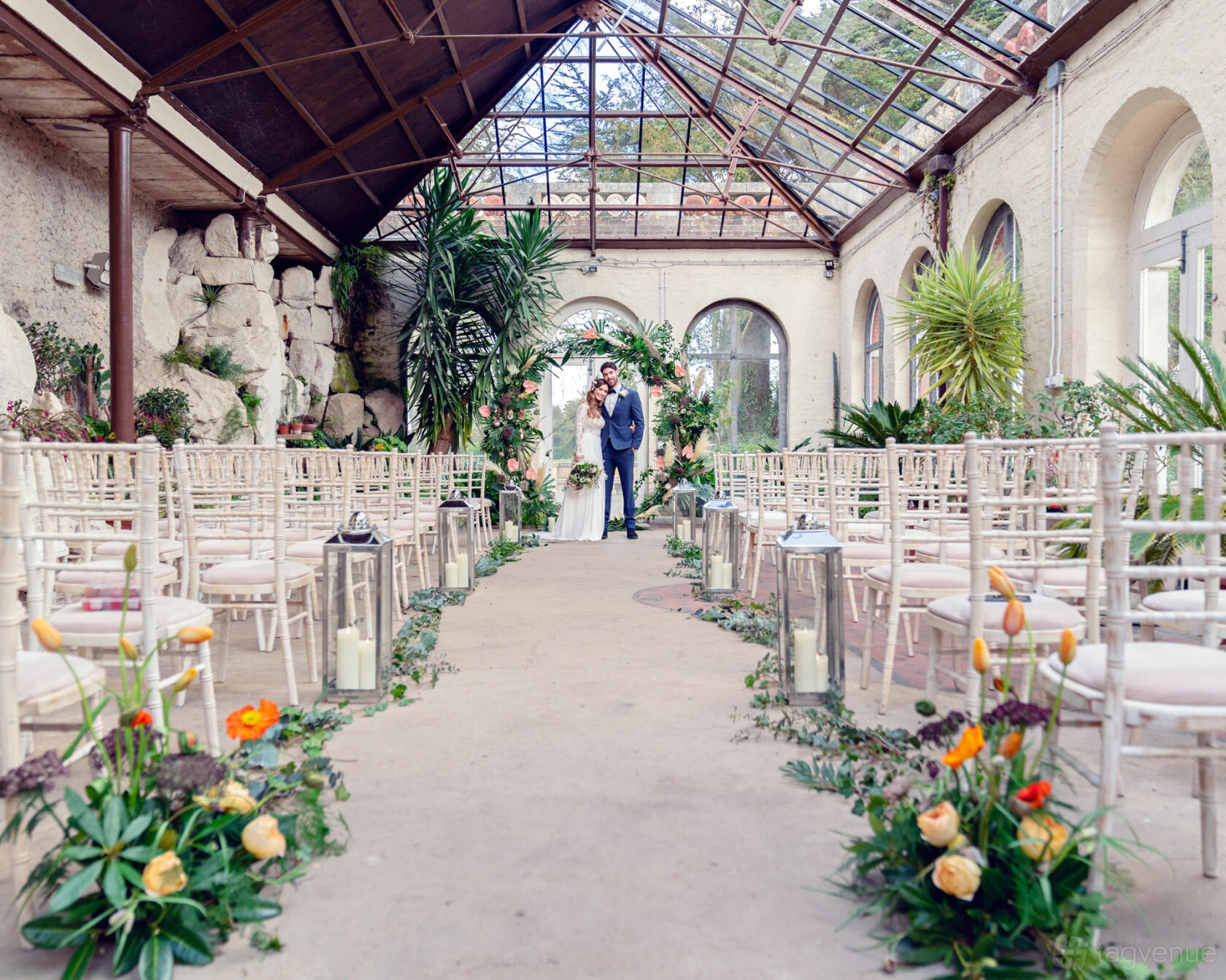 An event space with glass ceilings, stone walls, tropical plants, and rows of chairs at Ashridge House.
