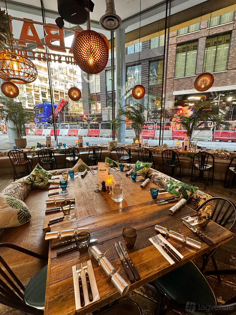 An event space in a restaurant with large windows, wooden tables, leafy cushions, and pendant lights at Cabana @ St Giles.