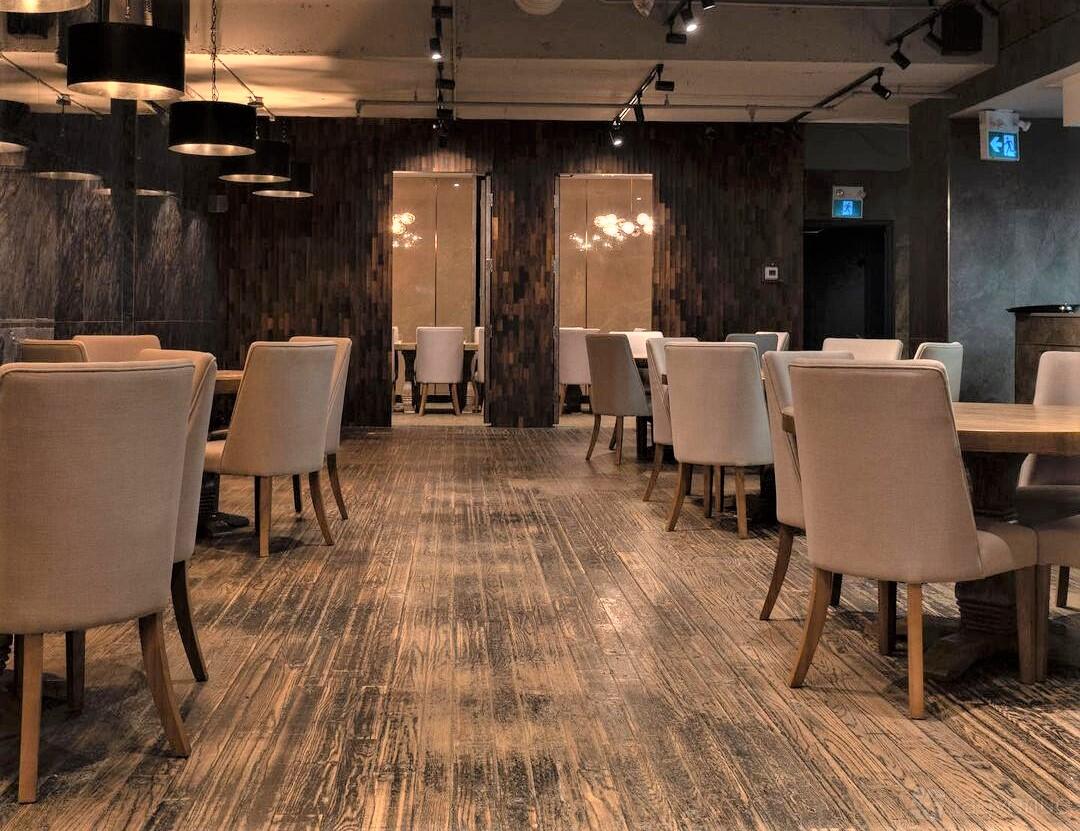 A restaurant with light upholstered chairs, wooden tables, pendant lighting, and textured wood flooring at Muni Robata.