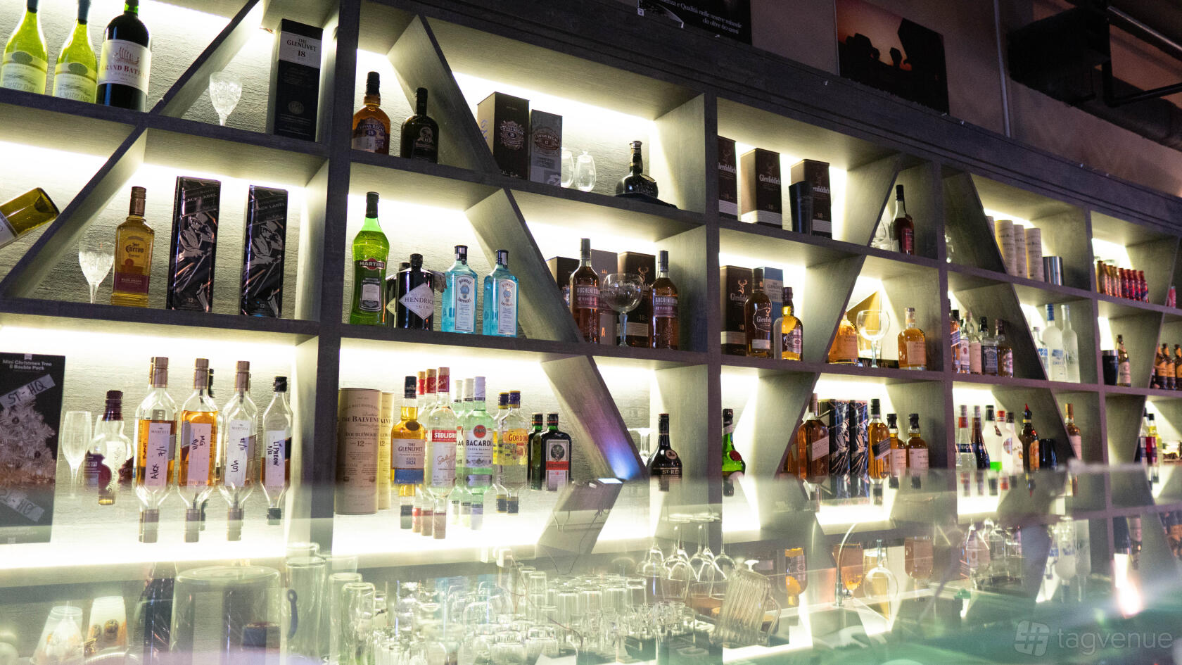 A bar in a restaurant with illuminated geometric shelves stocked with assorted spirits at Georges Hideout @ Seletar.