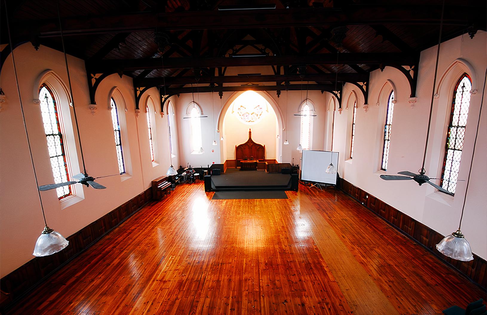 An event space with high arched windows, polished wooden floors, and exposed beams at Melbourne City Conference Centre.