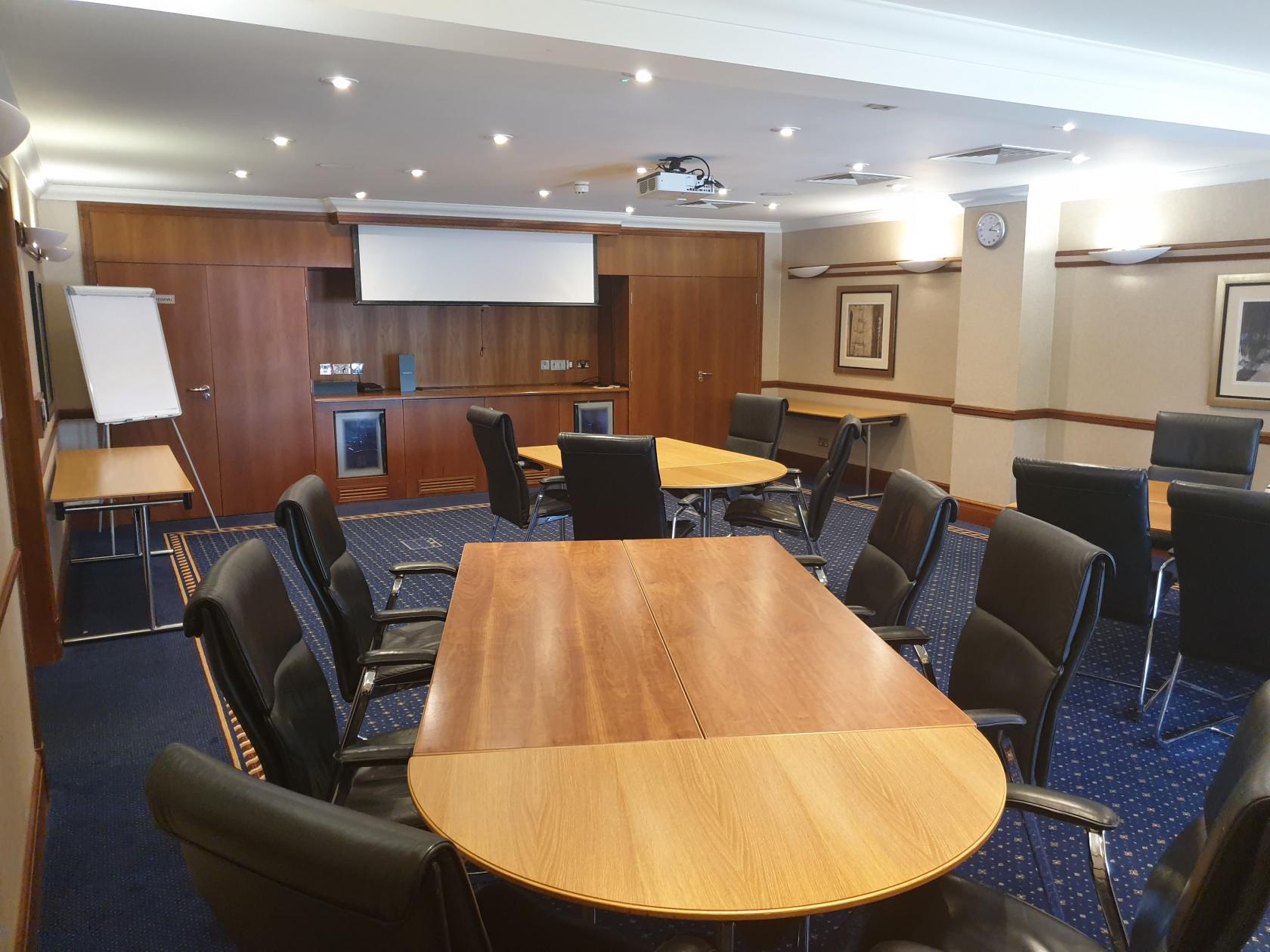 A meeting room with wood tables, black leather chairs, a flip chart, and a projector screen at Aztec Hotel & Spa.