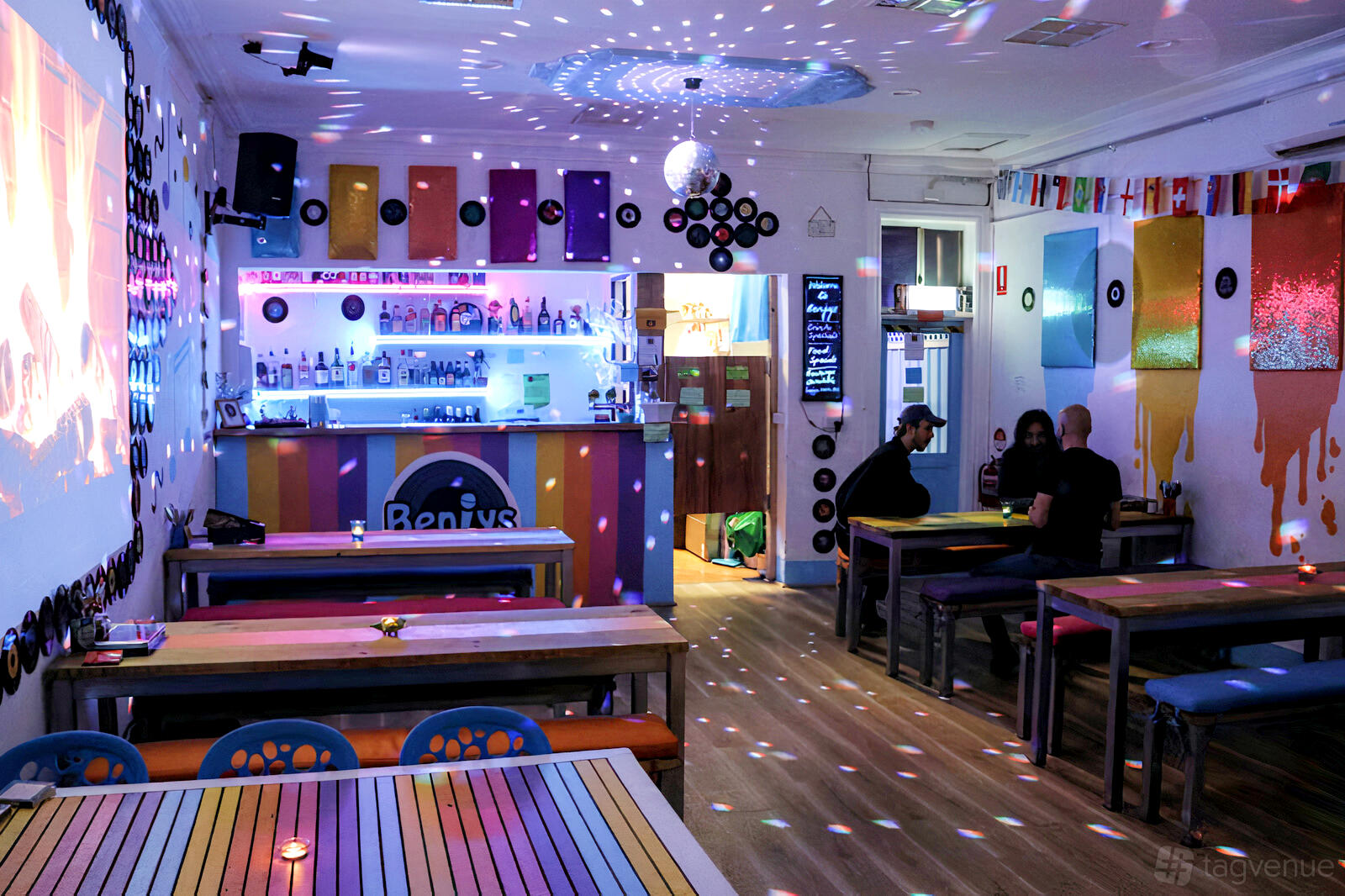 A karaoke bar with disco lights, wall-mounted vinyl records, colorful benches, and a neon-lit bar at Benjys Karaoke Bar.
