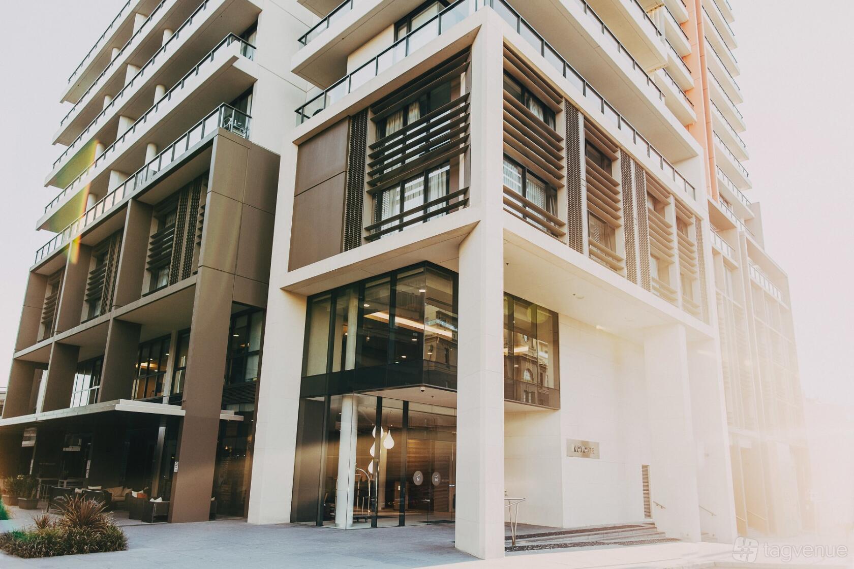 A hotel exterior with modern architecture, large windows, and outdoor seating at Novotel Newcastle Beach.