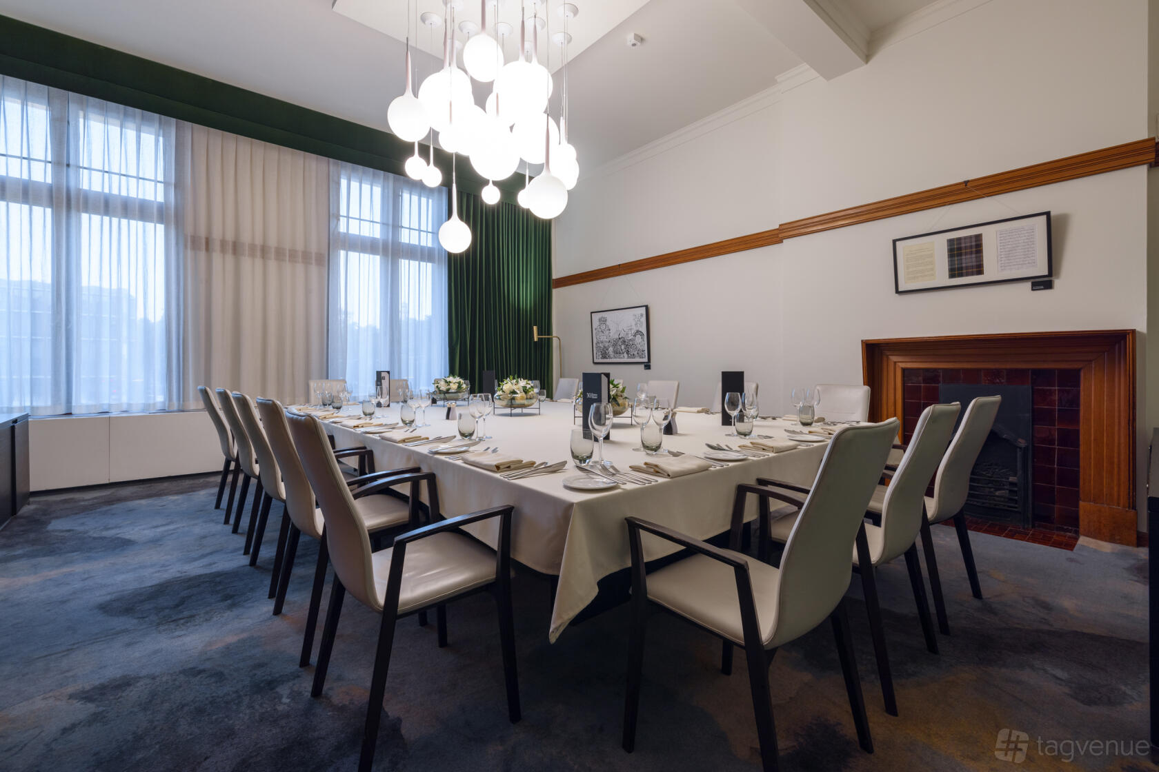 A dining room with a long table set for a formal meal, upholstered chairs, a modern chandelier, and tall windows at 30 Euston Square.