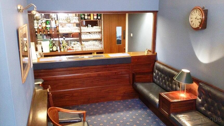 A bar with leather seating, wood-paneled counter, and glassware shelves at LMI Conference Centre.