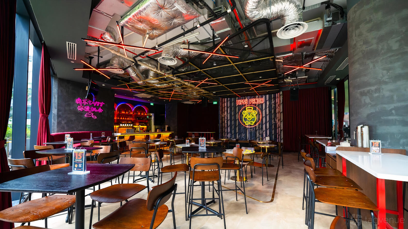 A pub with neon signs, exposed ductwork, wooden tables, and a colorful bar area at Tipsy Panda.