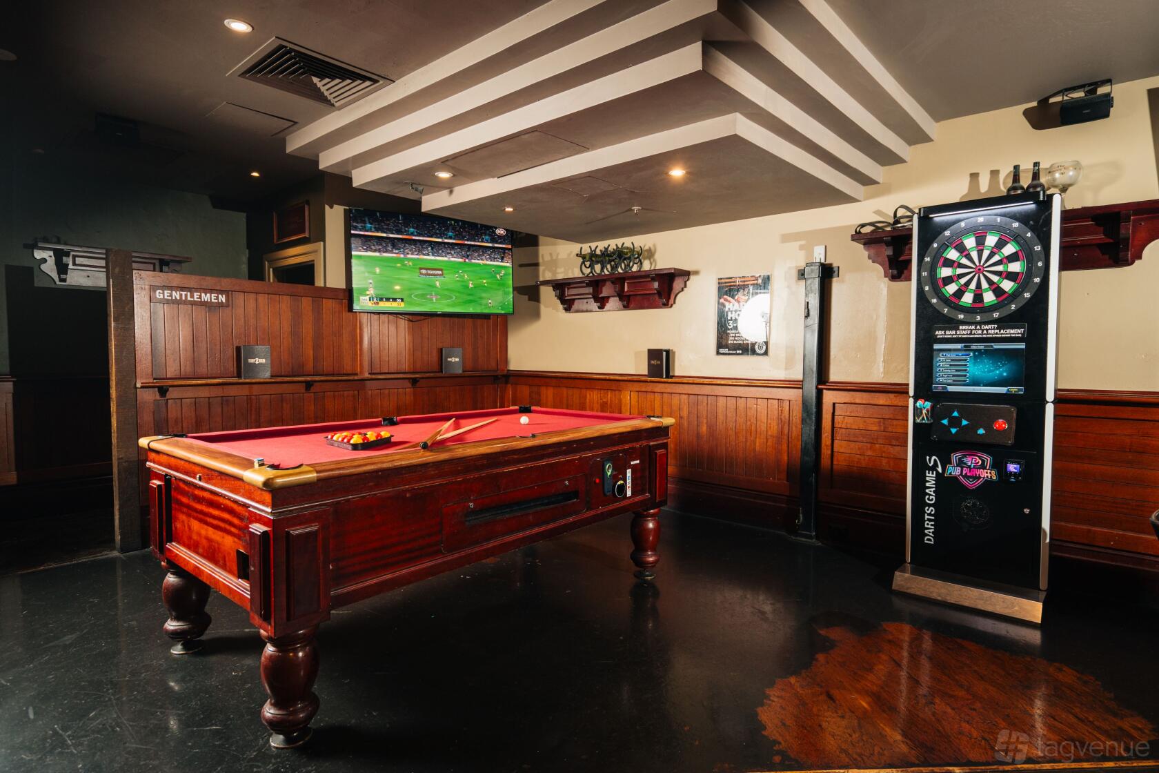 An event space in a bar with a red felt pool table, dartboard, and wall-mounted TV at Turf Bar.