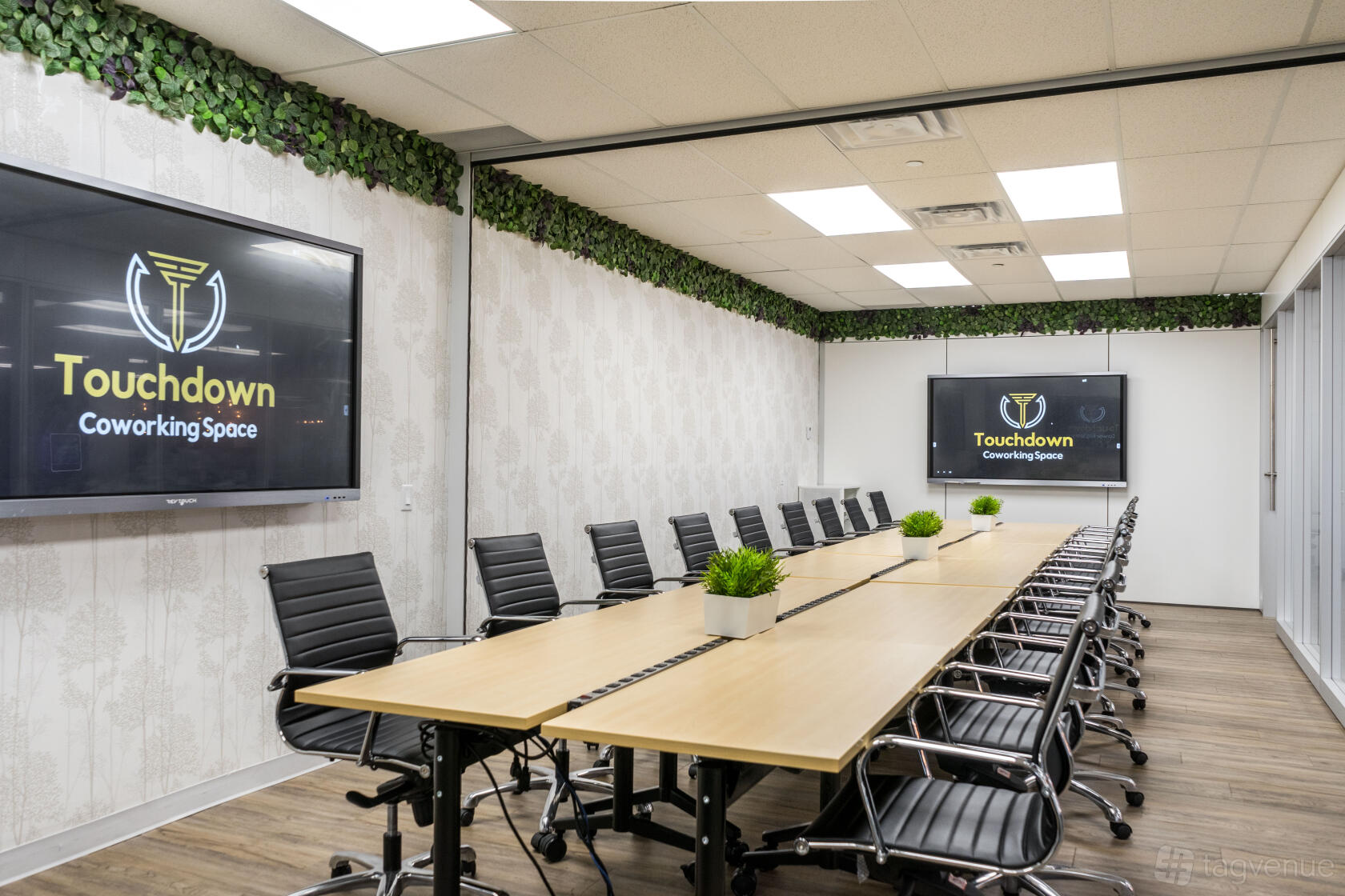 A coworking space with a long conference table, leather chairs, two large screens, and greenery accents at Touchdown Coworking.
