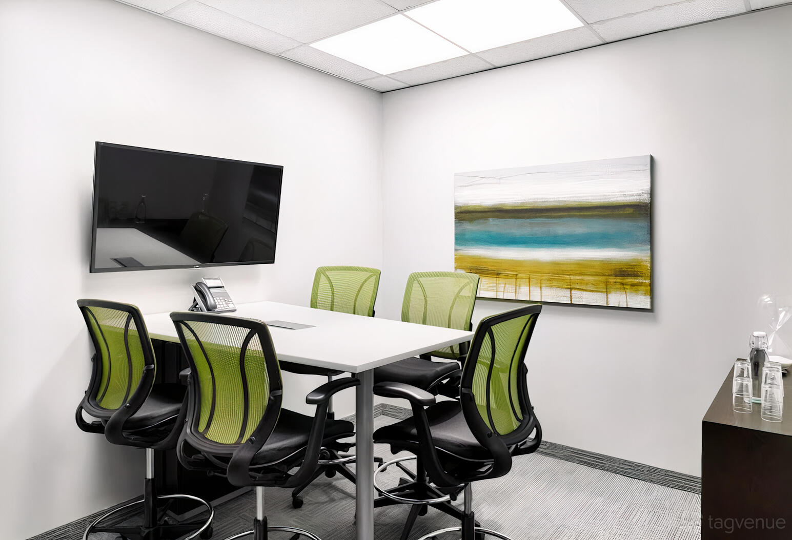 A meeting room with a rectangular table, green mesh chairs, wall-mounted TV, and abstract artwork at The Professional Centre.