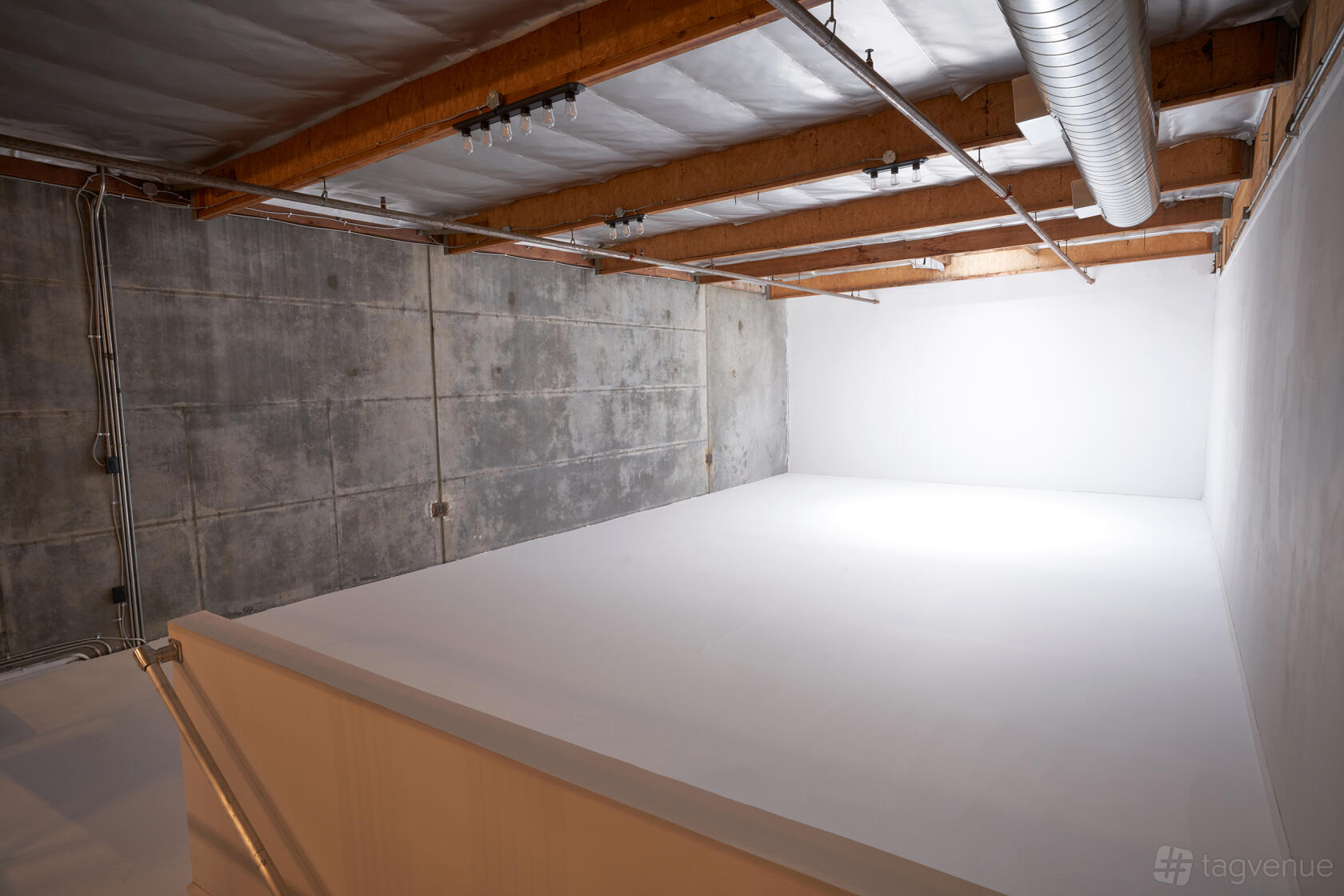 A photo studio with a seamless white cyclorama wall, exposed wooden ceiling beams, and concrete walls at Stay Lucky Studios.