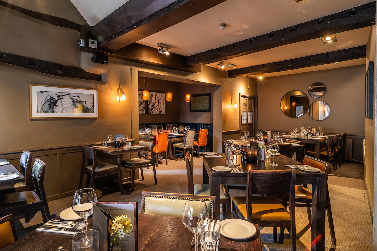 A dining room with exposed wooden beams, framed artwork, and set tables at The Royal Saracens Head.