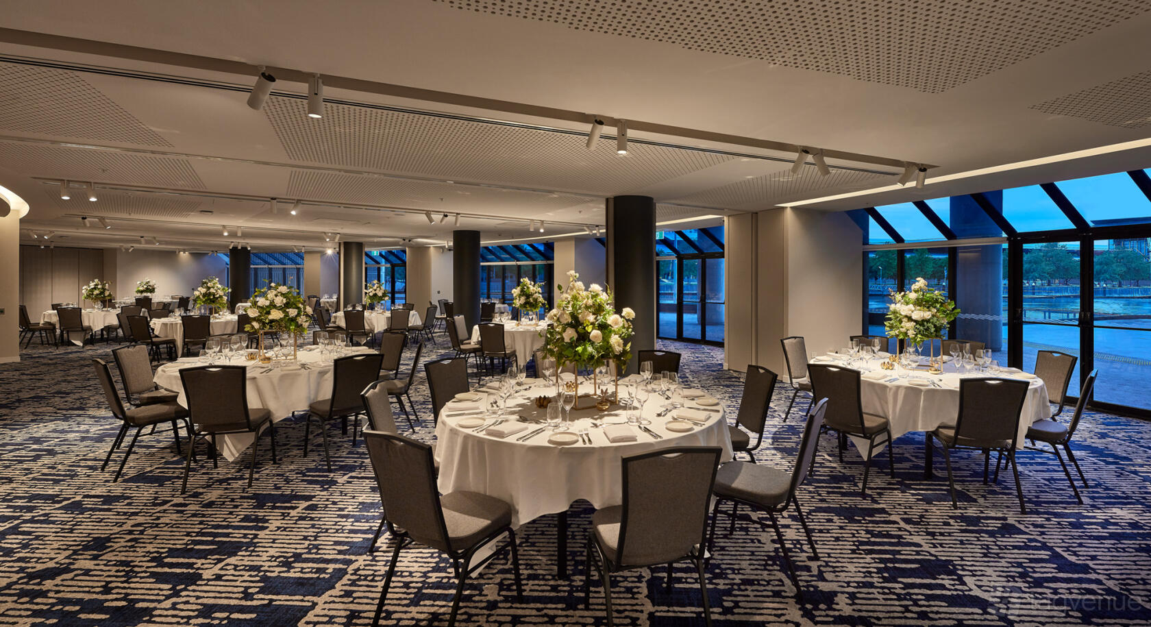 An event space in a hotel with round tables draped in white linens and large floral centerpieces at Pearl Riverfront.