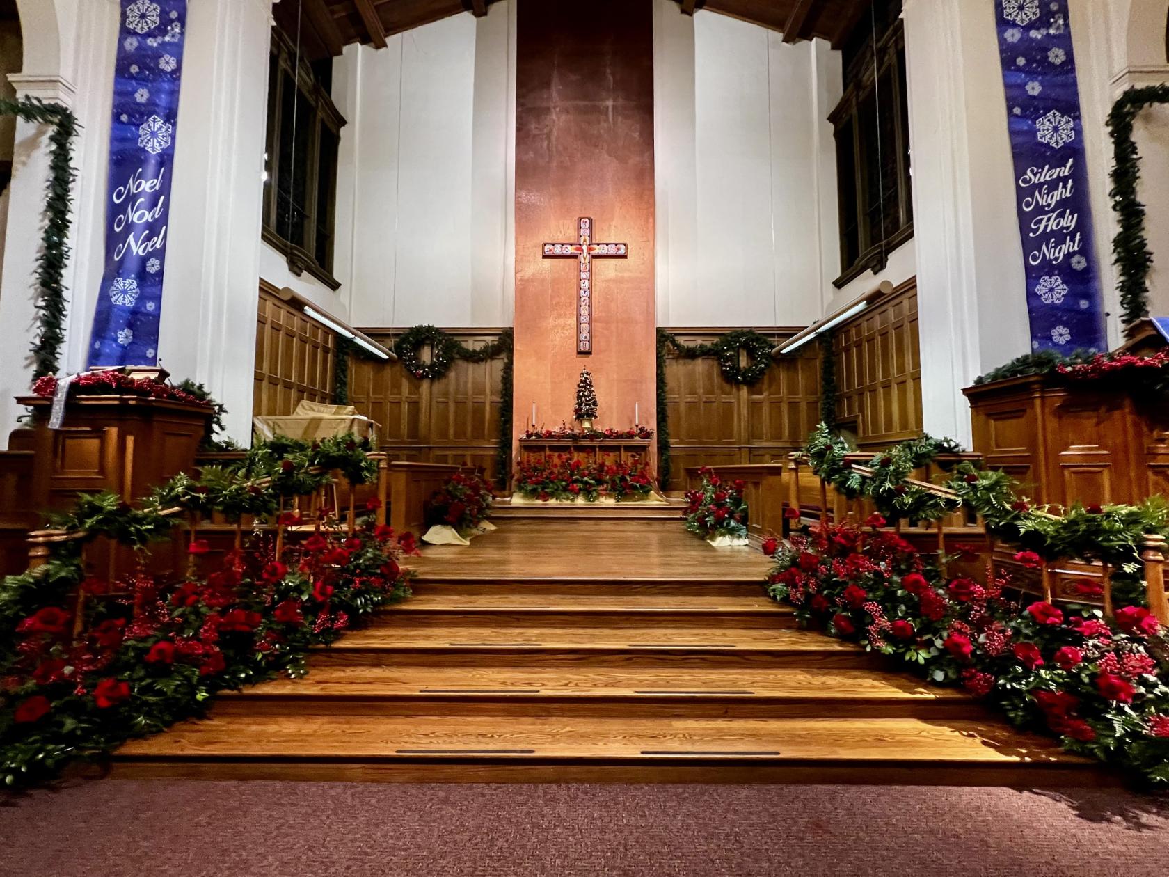 A church sanctuary with wooden pews, festively decorated railings, and a large cross at First Congregational Church of Riverside.