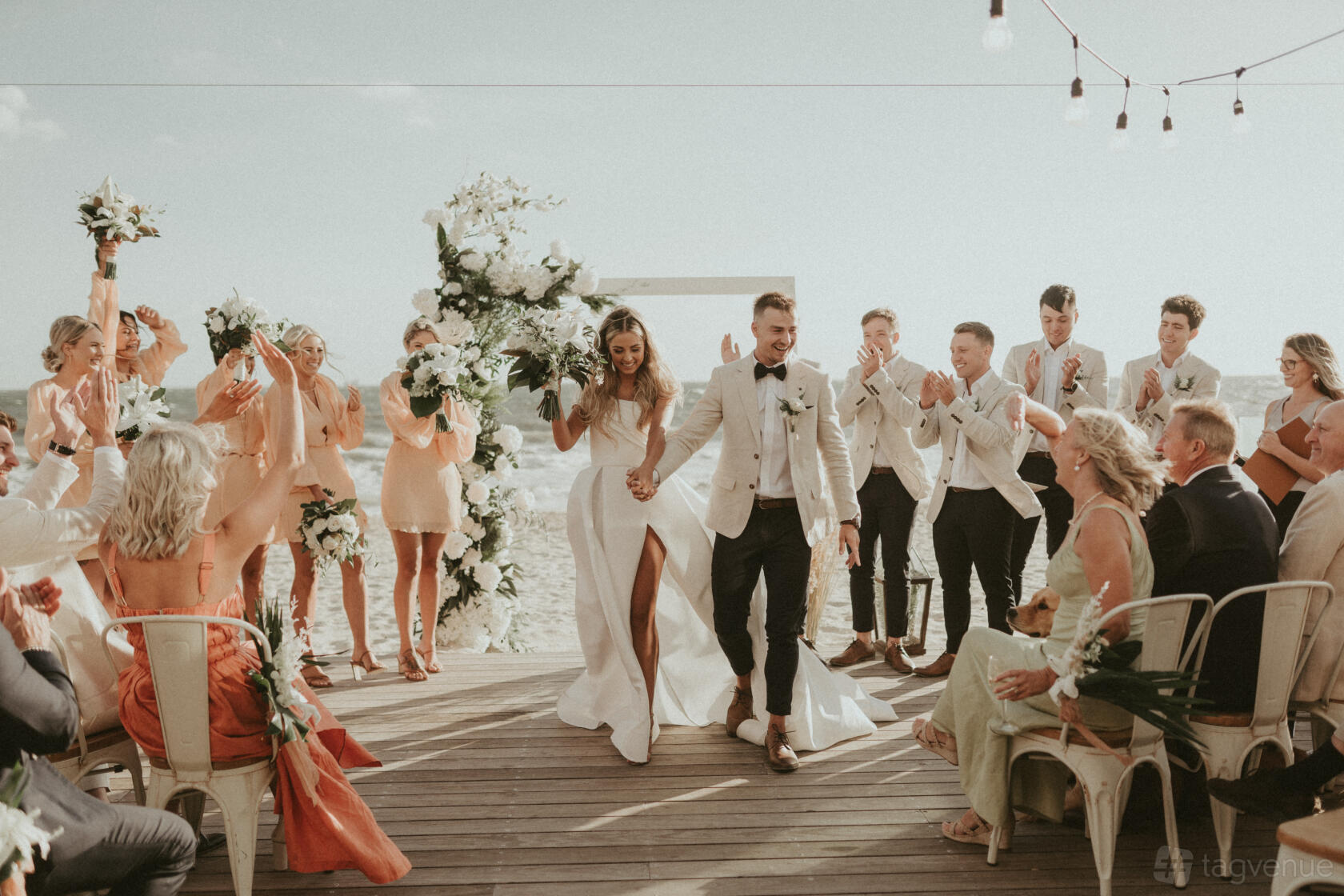 A beachfront cafe with wooden decking, white metal chairs, and string lights at The Sandbar.