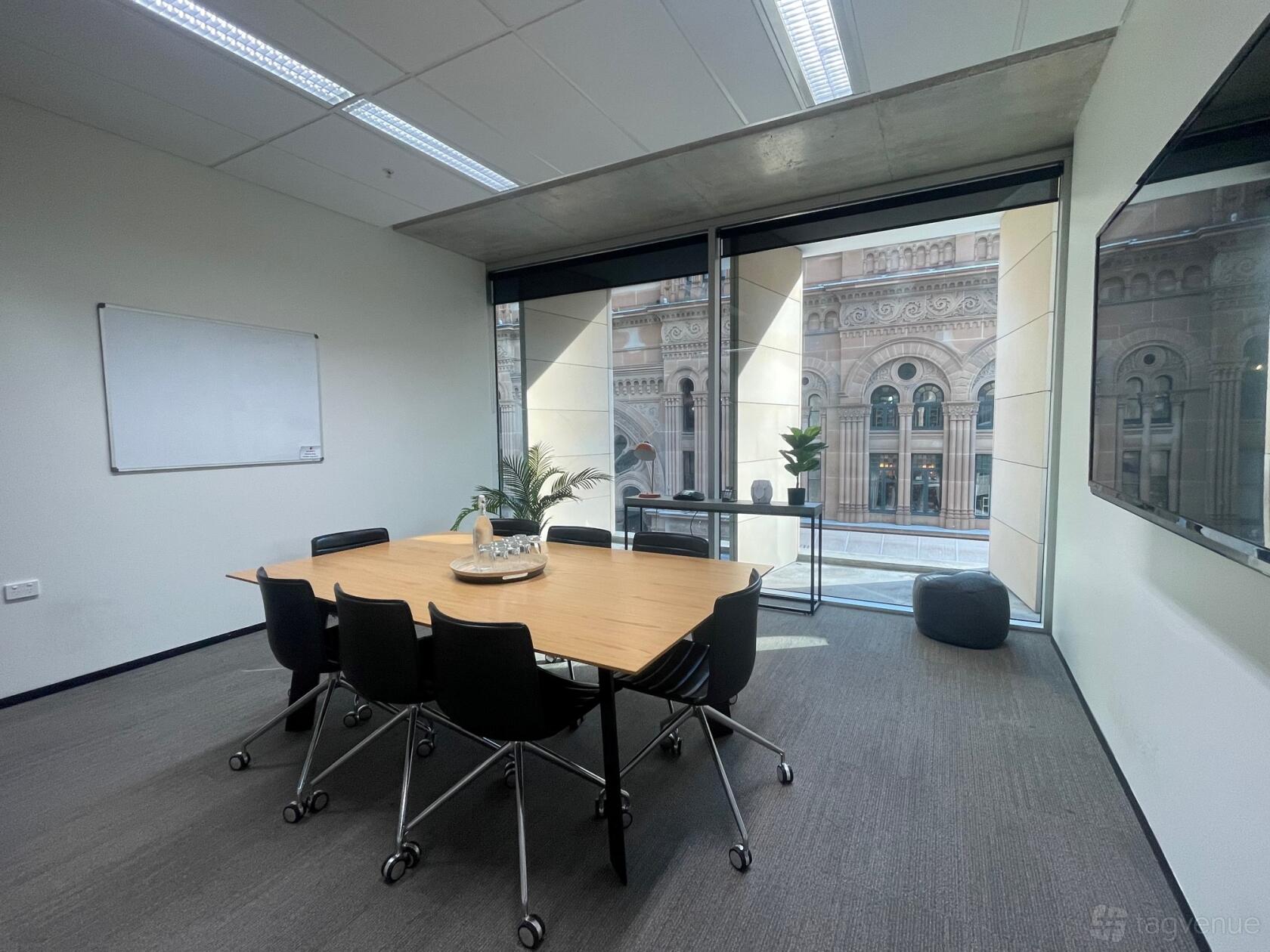 A boardroom with a rectangular table, black chairs, floor-to-ceiling windows, and a whiteboard at Edge Offices.