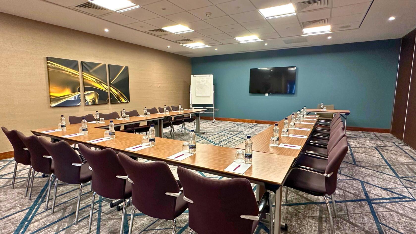 An auditorium with U-shaped tables, bottled water, notepads, and a wall-mounted screen at Crowne Plaza Reading.