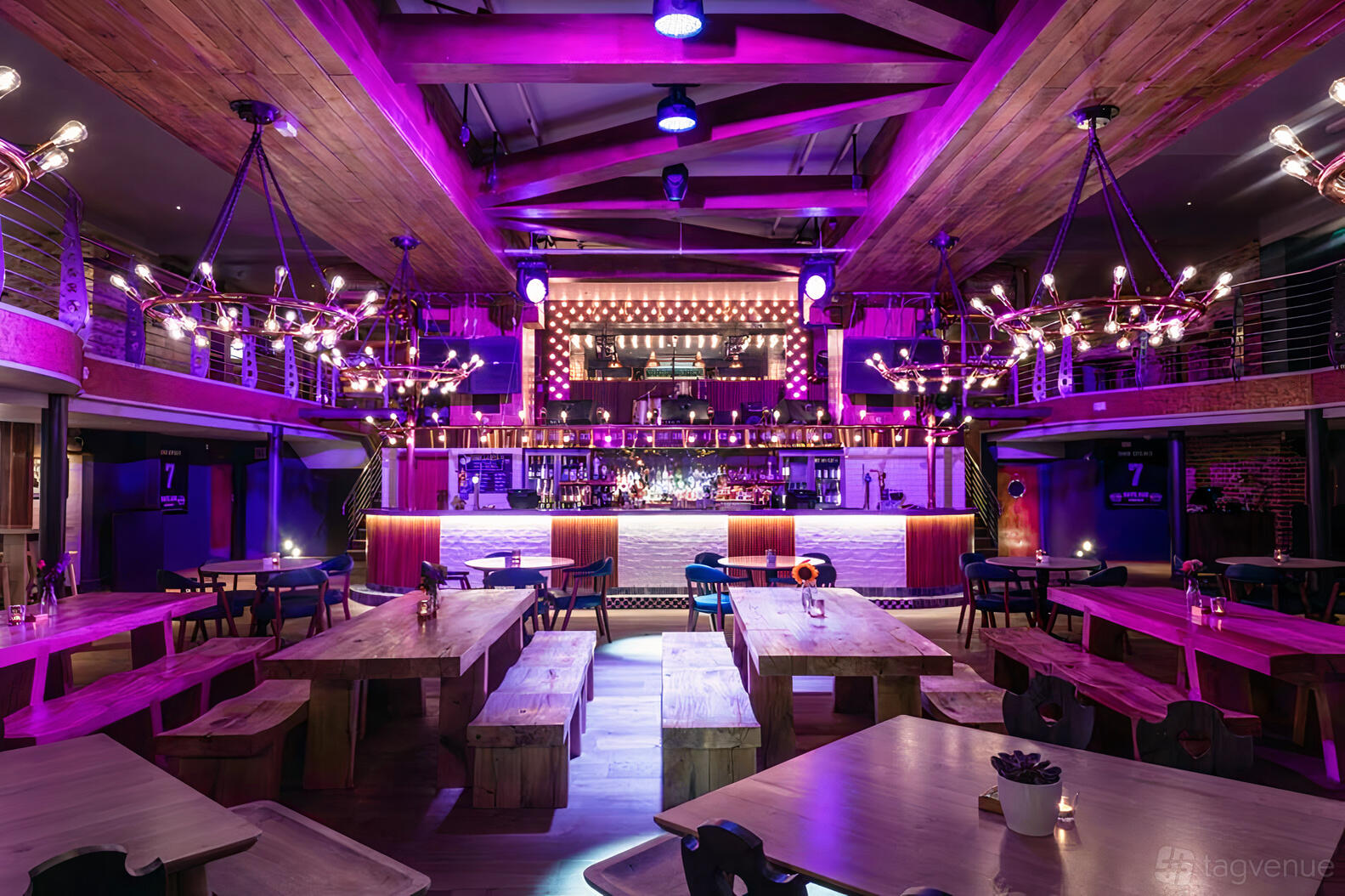 An event space in a restaurant with long wooden tables, bench seating, and colorful stage lighting at Brewhemia.