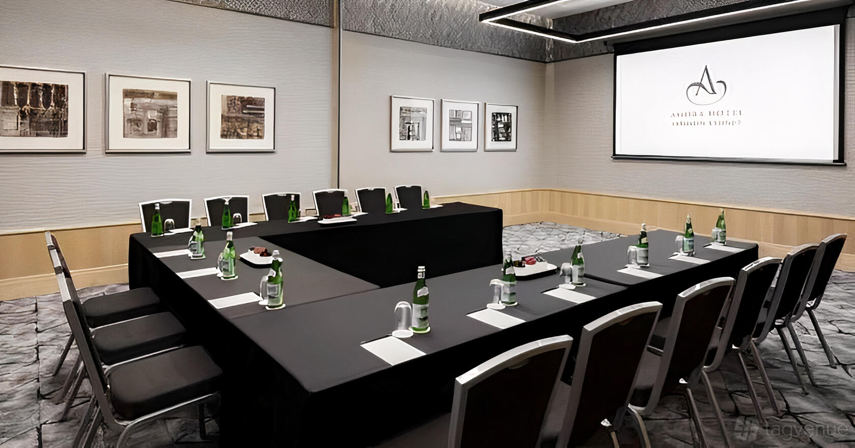 A hotel meeting room with a U-shaped table arrangement, bottled water, notepads, and a projection screen at Amora Hotel Jamison Sydney.
