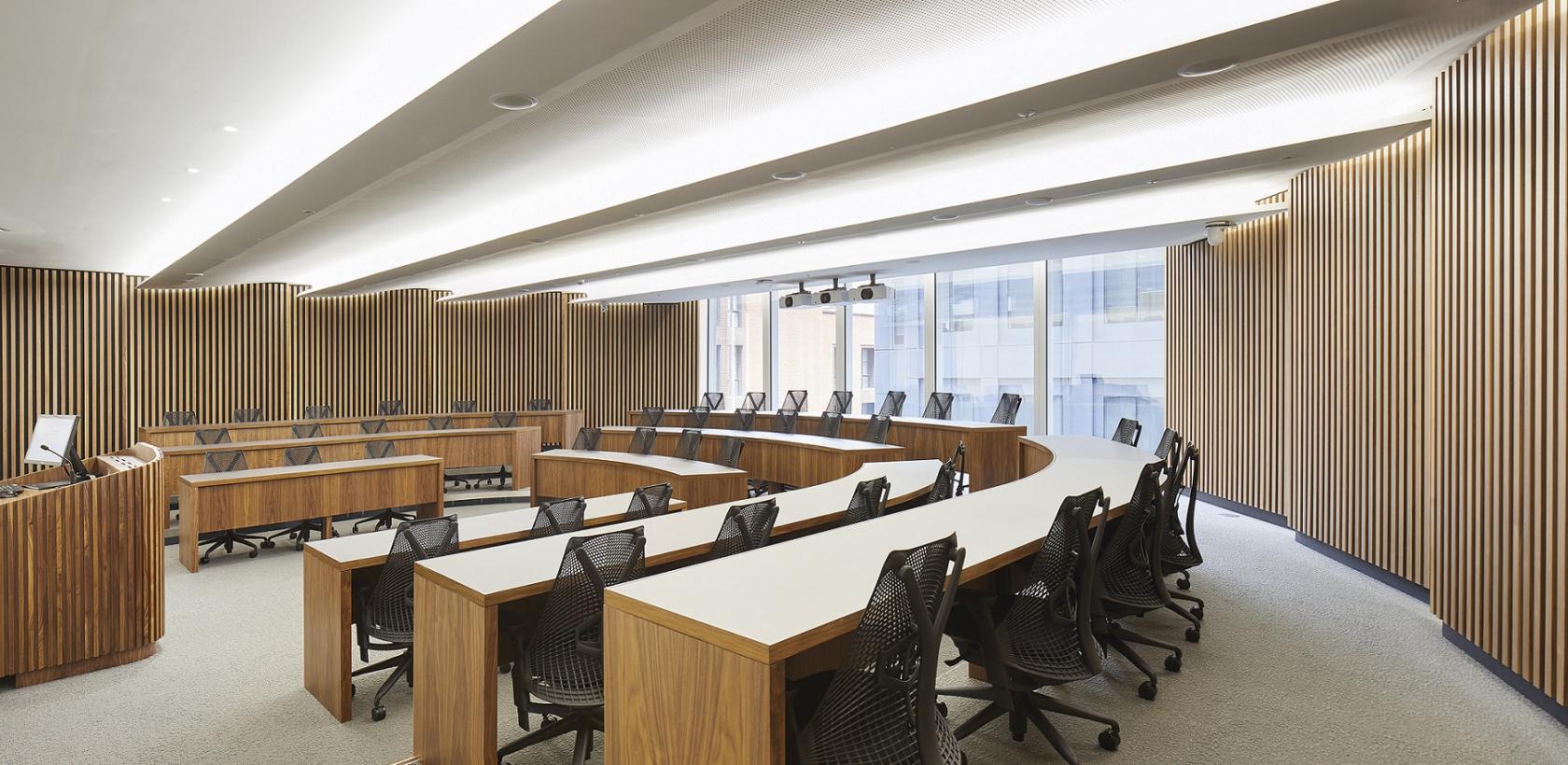 A training room with curved wooden tables, ergonomic chairs, and floor-to-ceiling windows at London Conference Centre.
