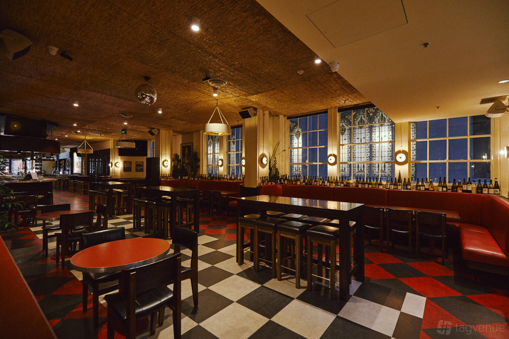 A pub lounge with checkered floors, red booths, dark wood tables, and large windows at Natural History Public Bar.